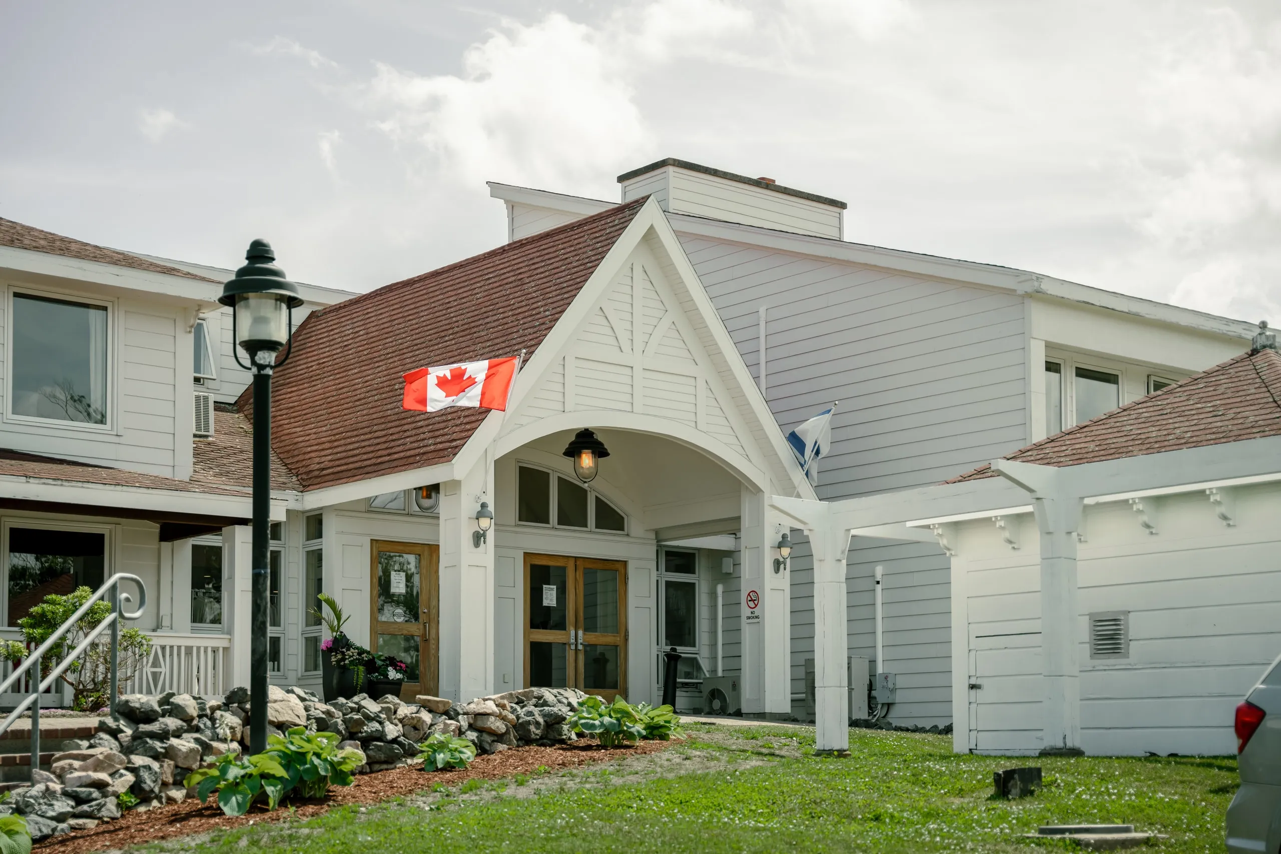 The white gabled entrance of The Corson House, with a Canadian flag under the portico and a stone garden in front.