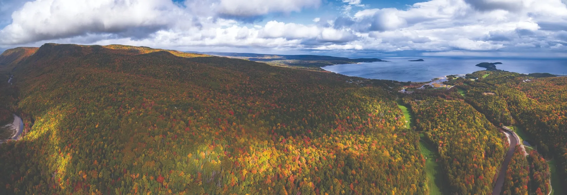 Aerial view of autumn forest along the Cabot Trail, with a lake and the coast beyond.