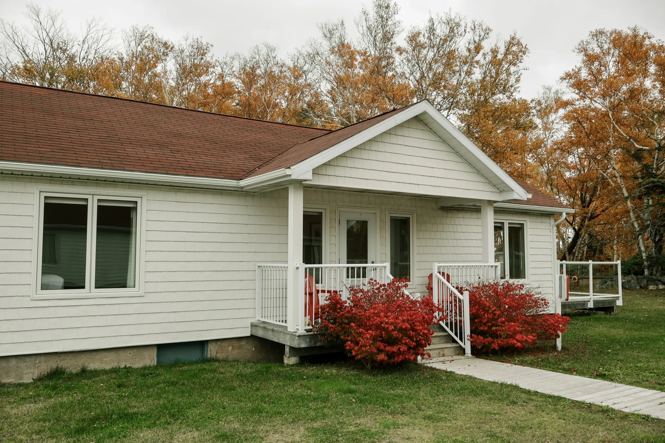 The white-shingled exterior of a Courtyard suite with a small porch, red landscaping, and autumn trees behind.