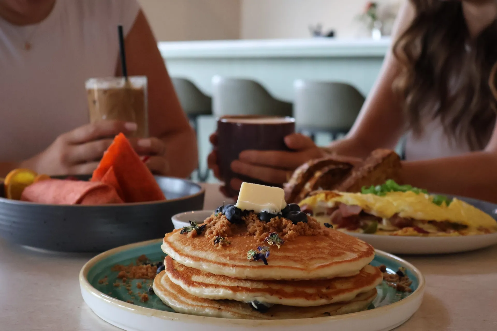 Pancakes with butter and berries on a breakfast table, with iced coffee, an omelette, and guests at The Arduaine.