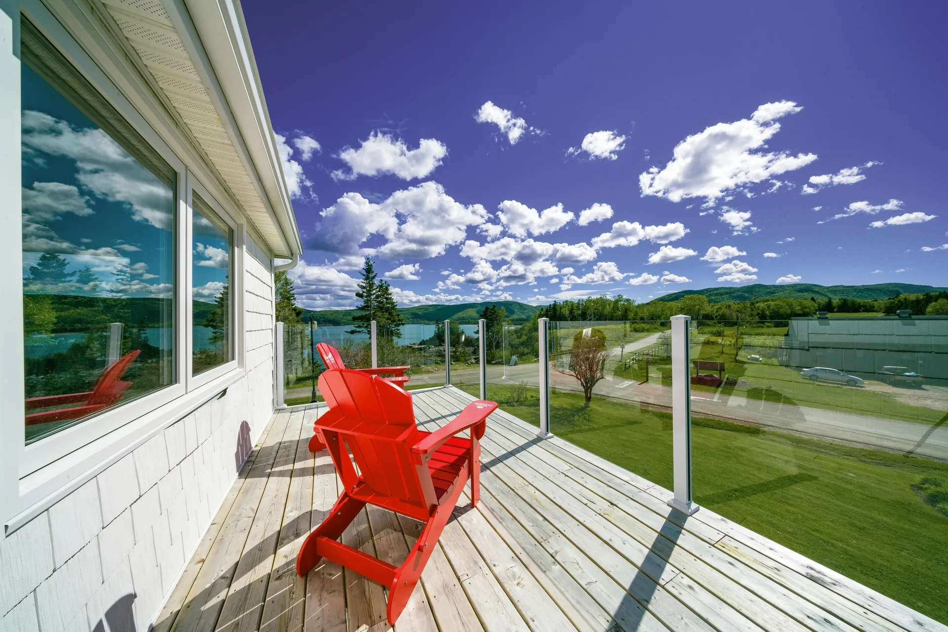 A red Adirondack chair on a wooden deck looking over a lawn toward the water and hills.