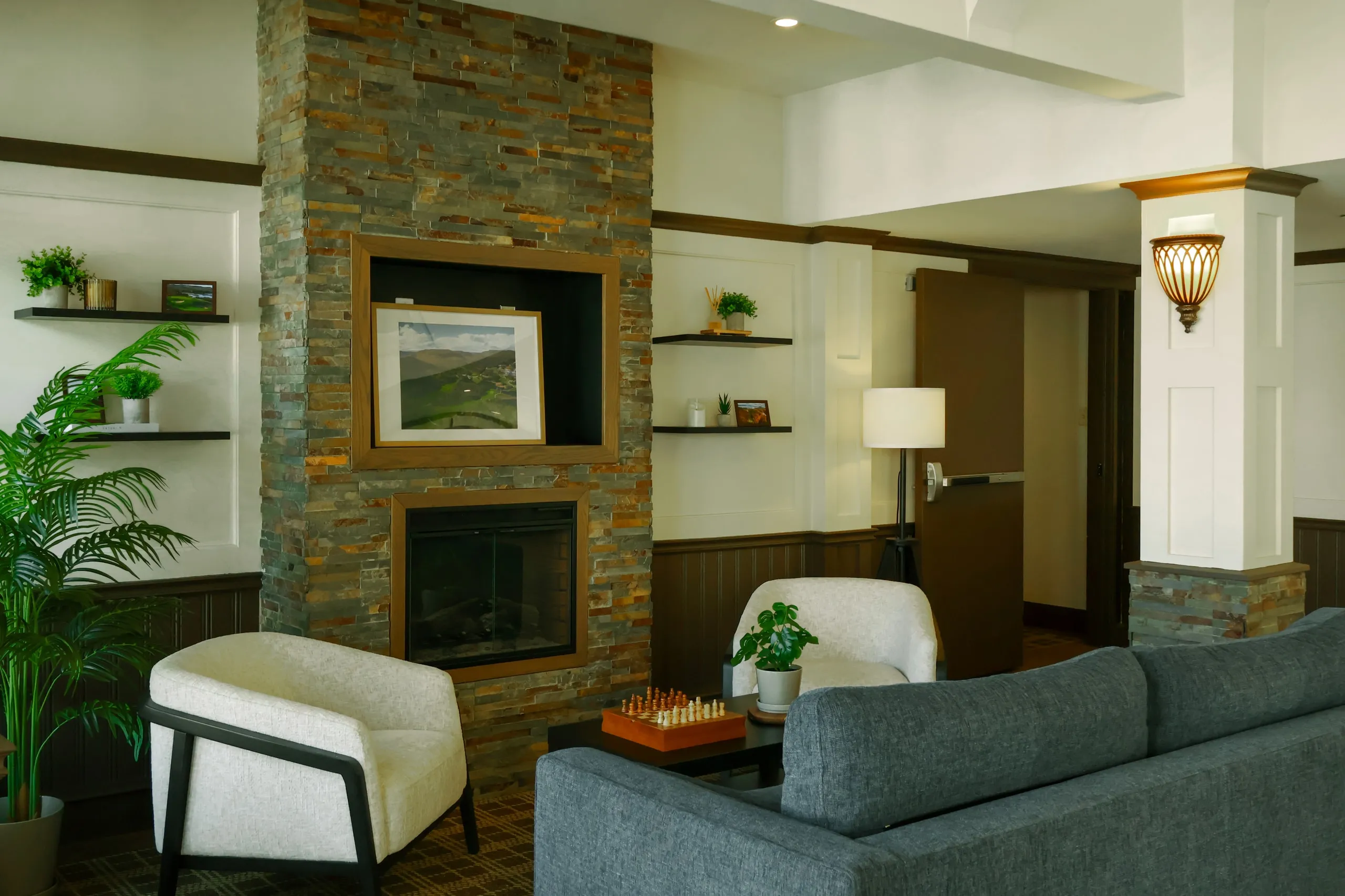 A lounge with a stone fireplace, a grey sofa, and a chessboard on the coffee table.