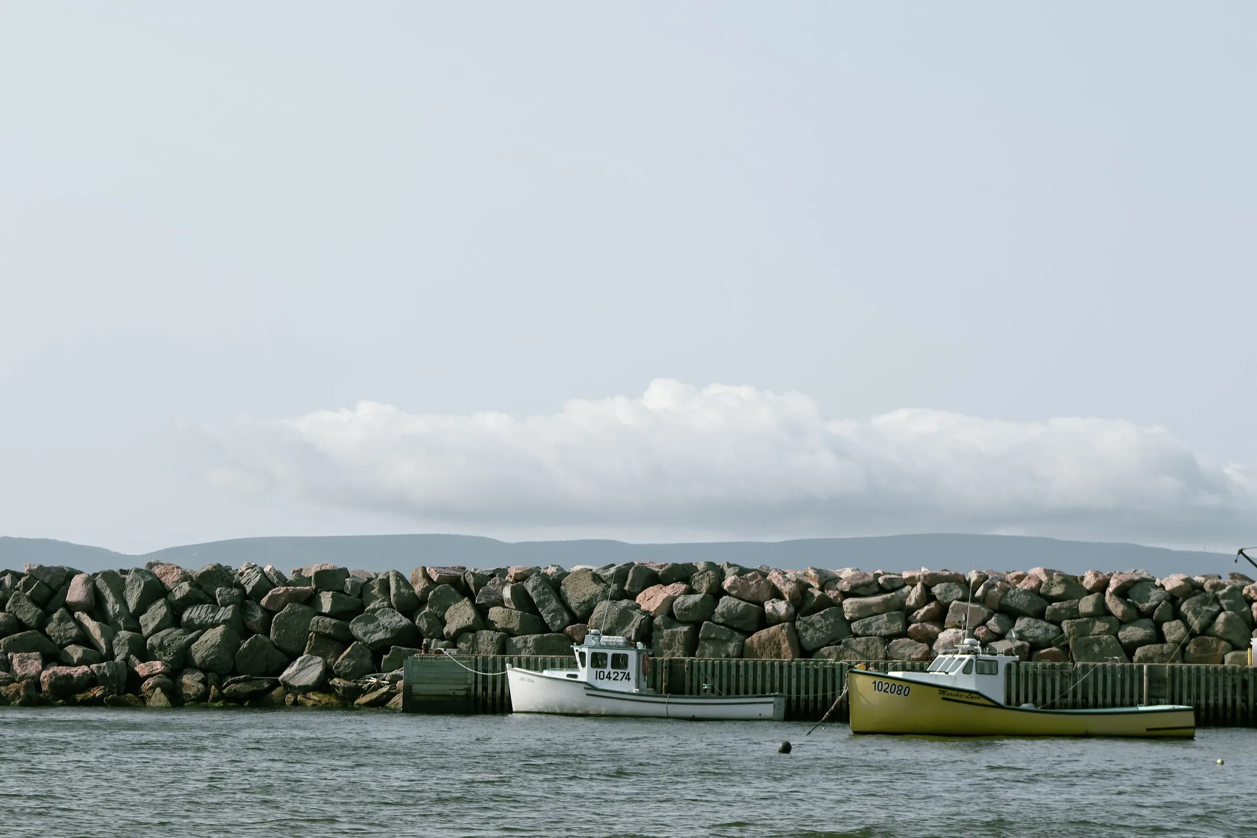 Two small boats moored beside a stone breakwater under a pale sky.