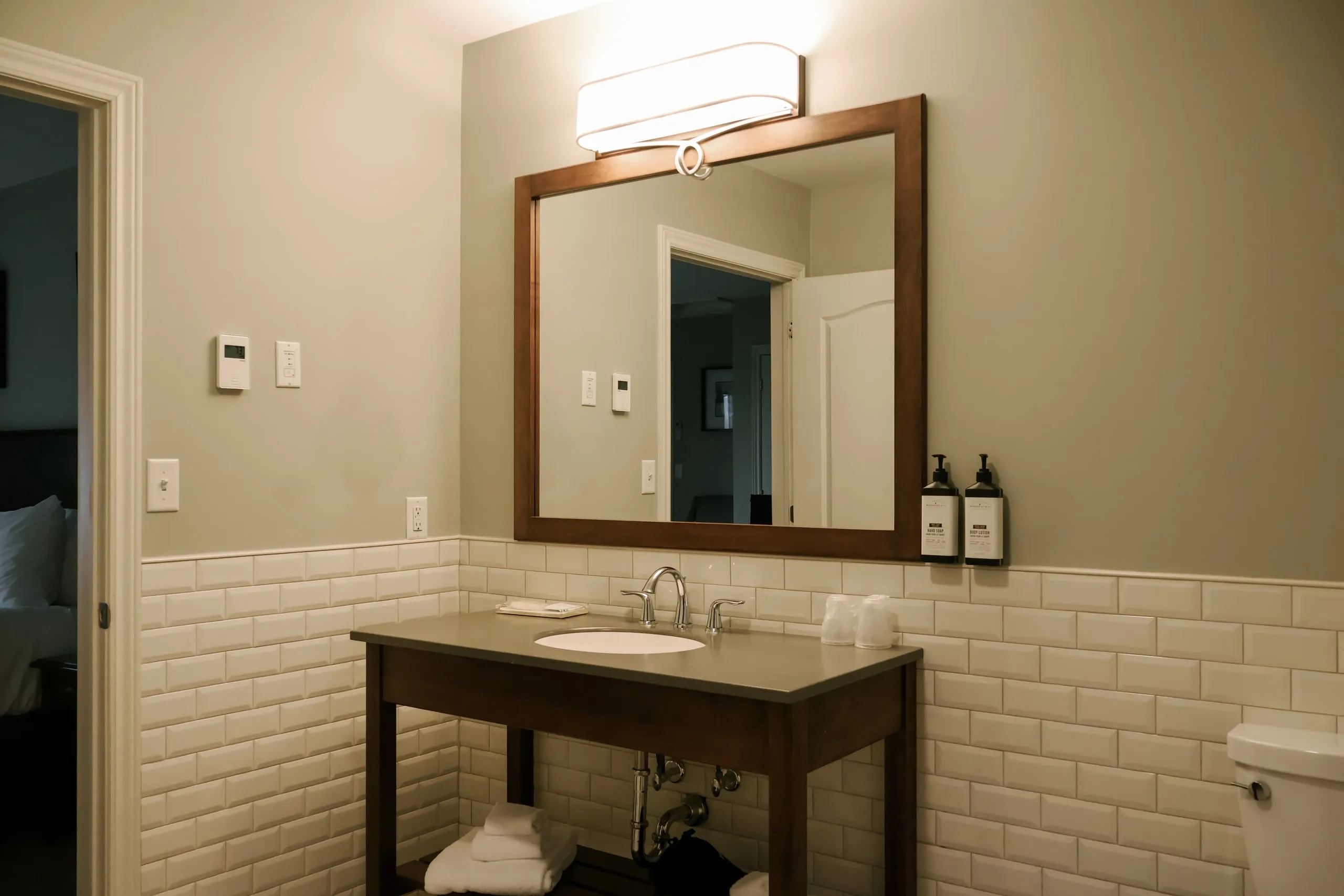 An ensuite bathroom with white subway tile, a dark wood vanity, and a mirror reflecting the bedroom doorway.