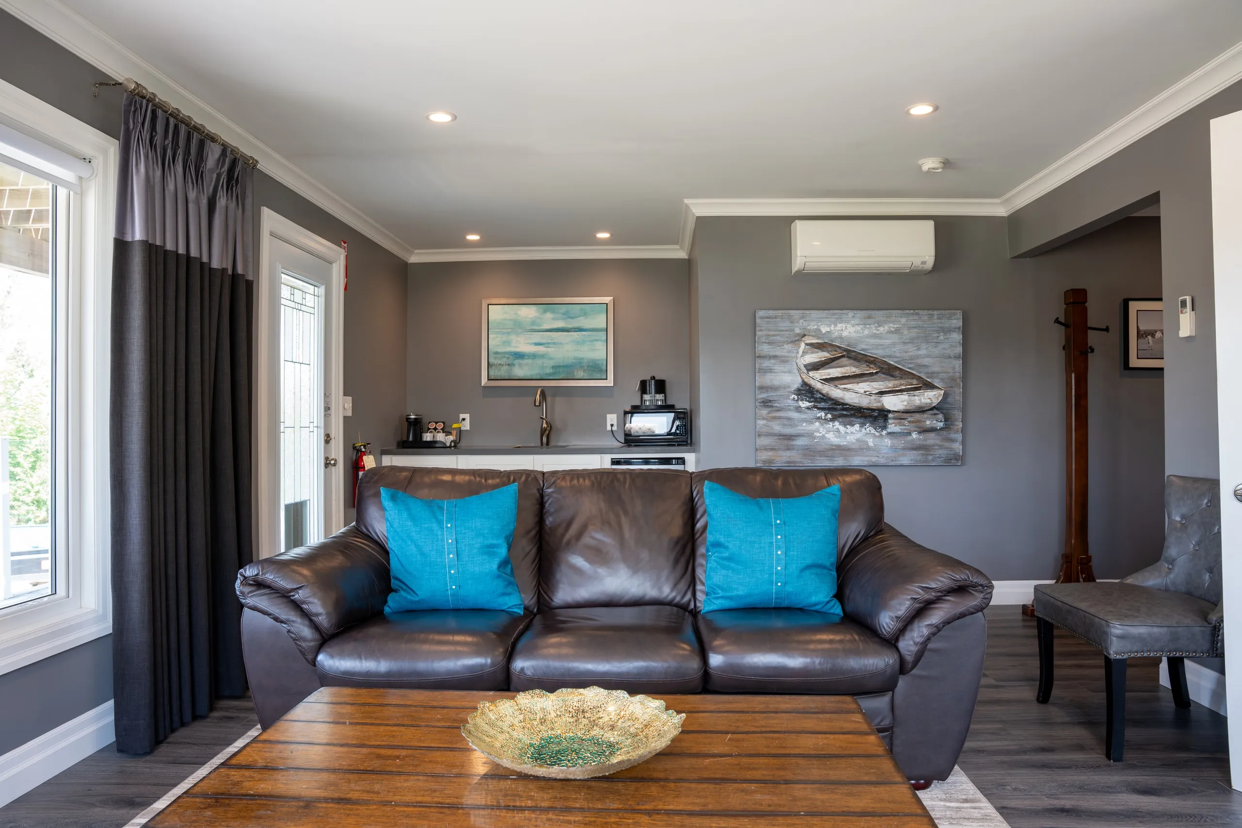 A dark leather sofa with turquoise pillows beneath wall art of a rowboat in a grey living room.