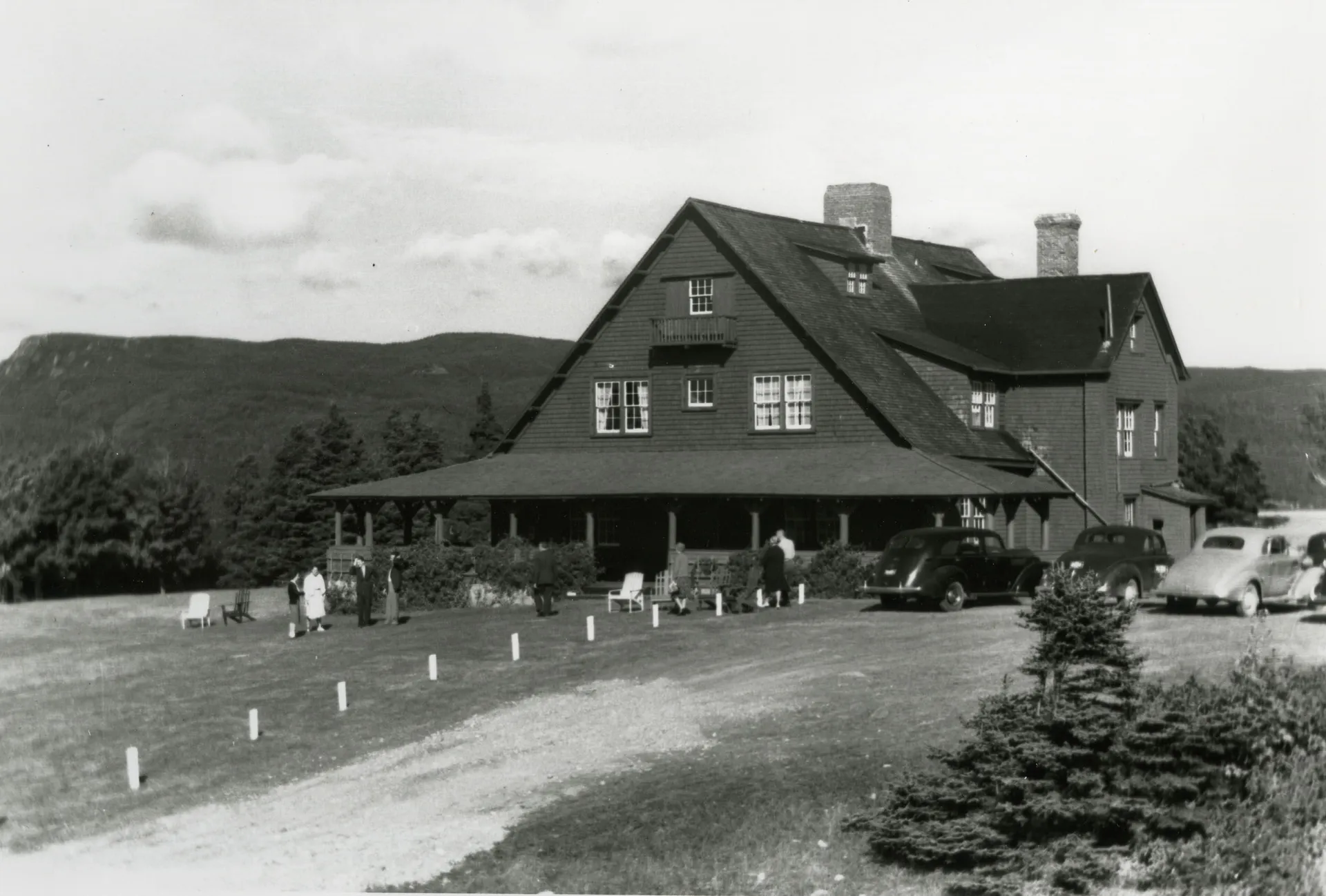 A large dark rustic lodge with a wide porch and multiple gables in a black-and-white archival photograph.