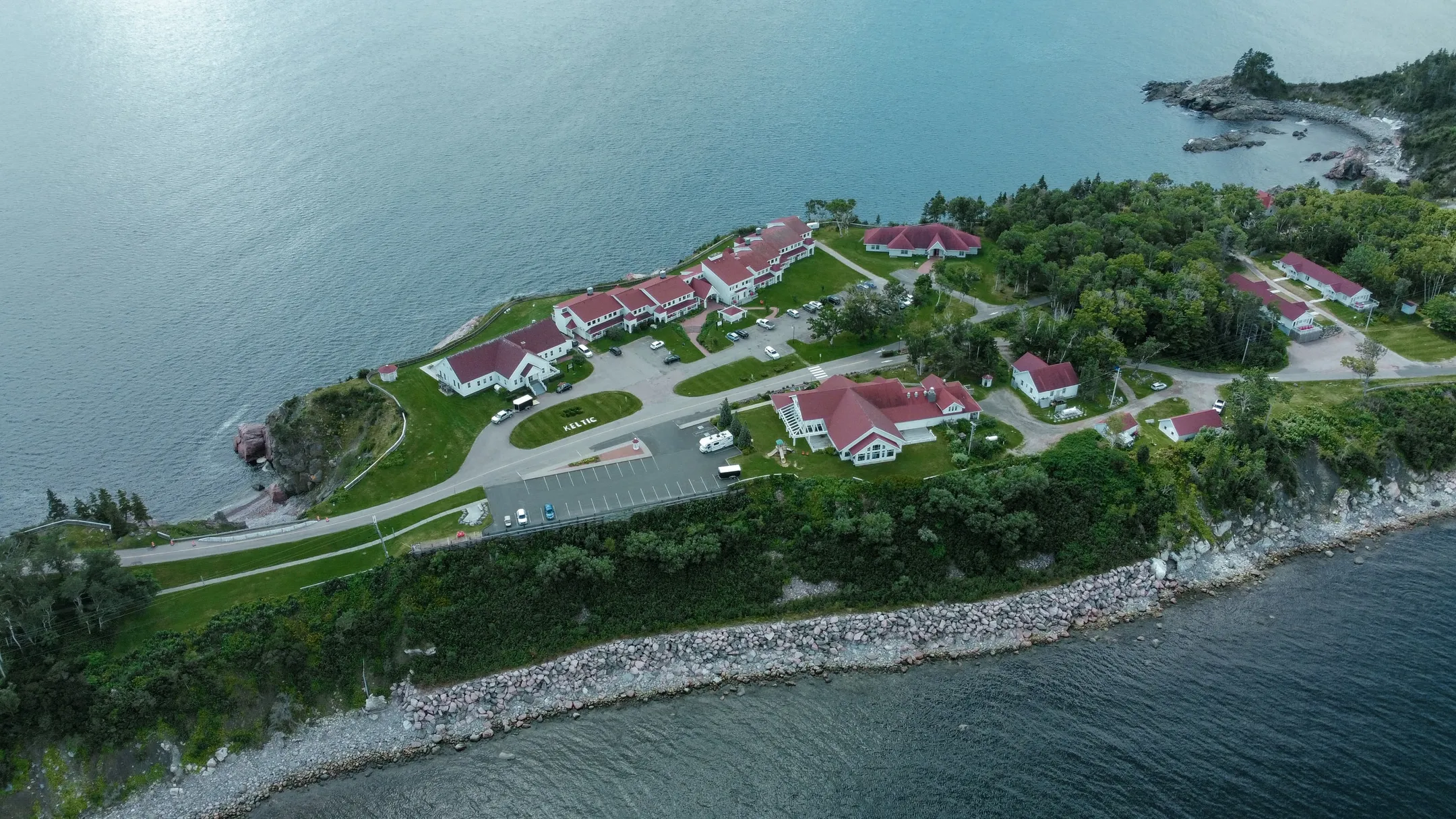 An aerial view of red-roofed resort buildings along a rocky, forested coastline.