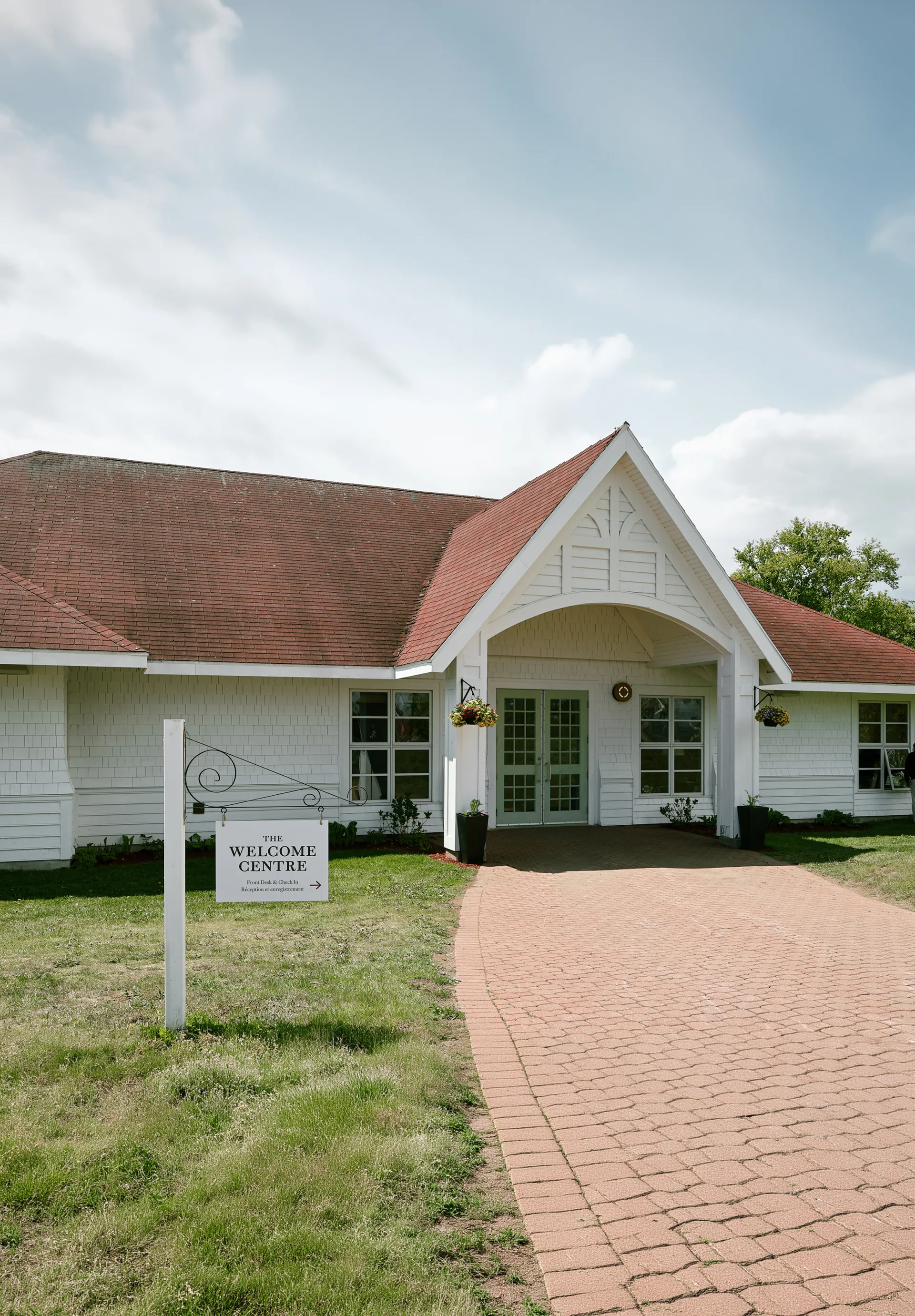 White-shingled Welcome Centre entrance with a red-tiled roof, green doors, and a brick path.