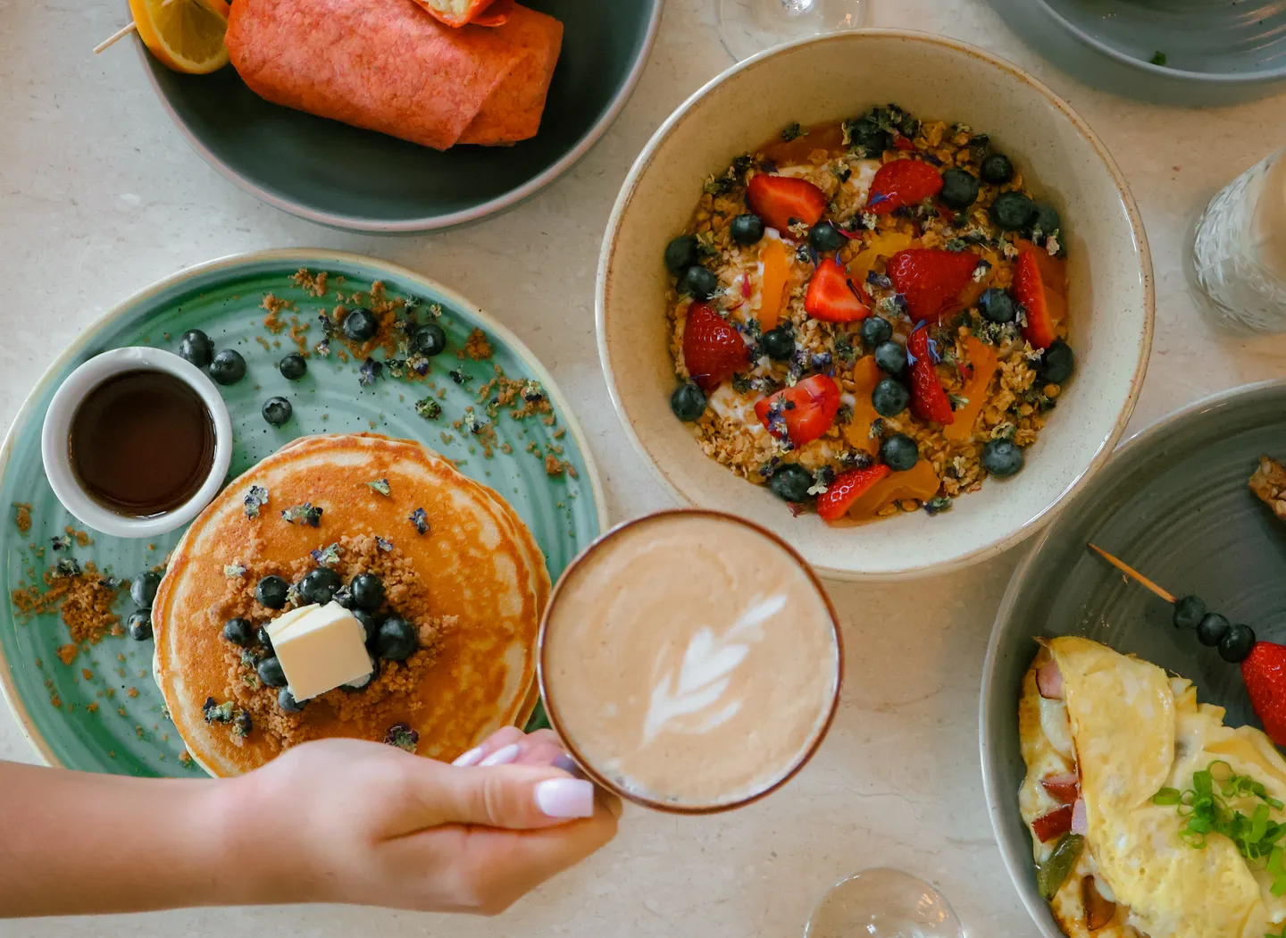 Pancakes, granola, and a latte on a breakfast table
