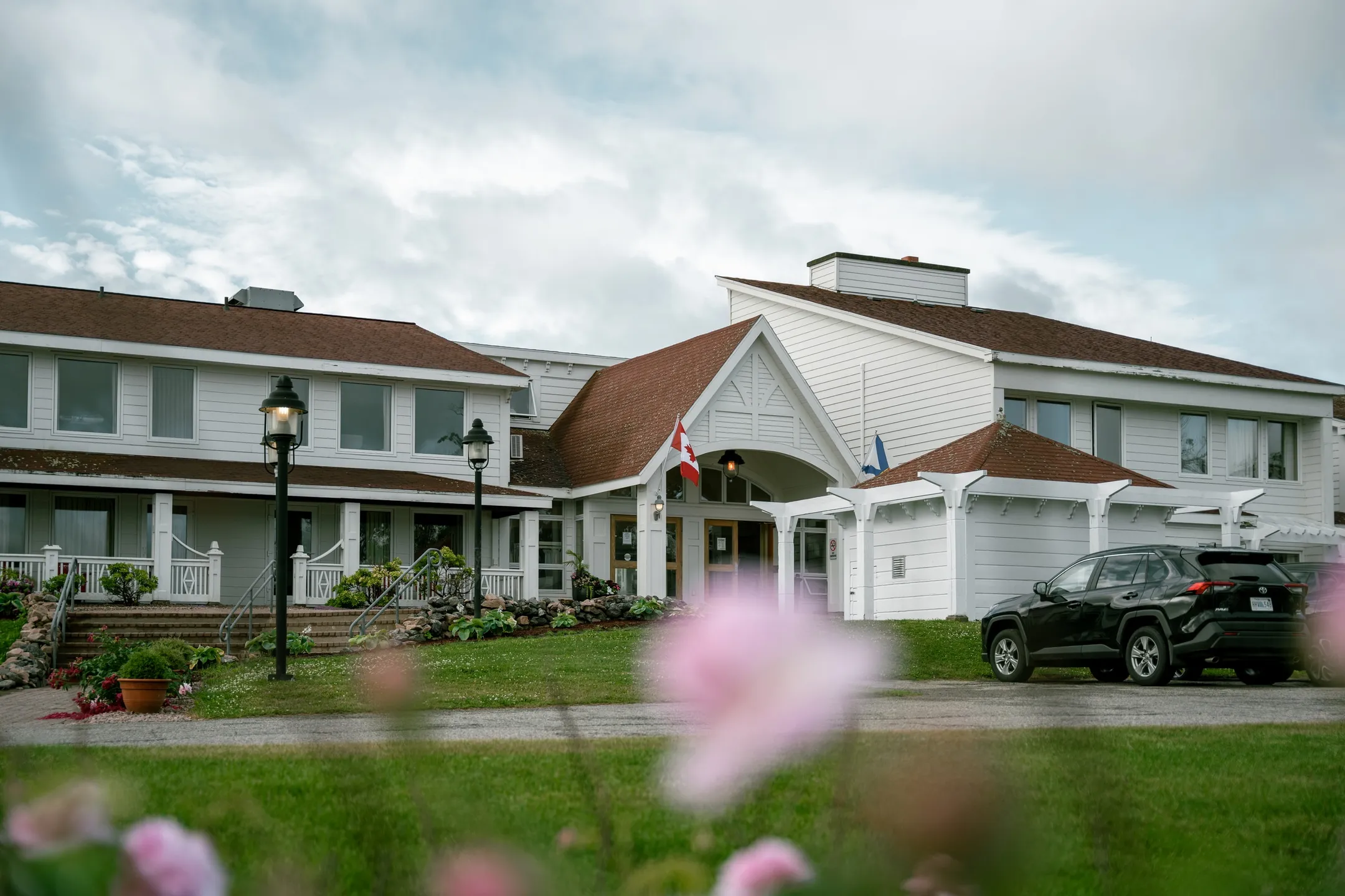 The white gabled entrance of The Keltic Resort, with lampposts, flower beds, and a vehicle parked along the drive.