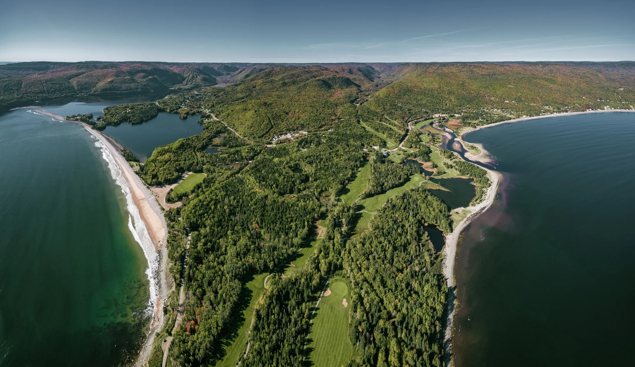 Aerial view of Highlands Links fairways winding through forest between the Atlantic and a sandy beach.