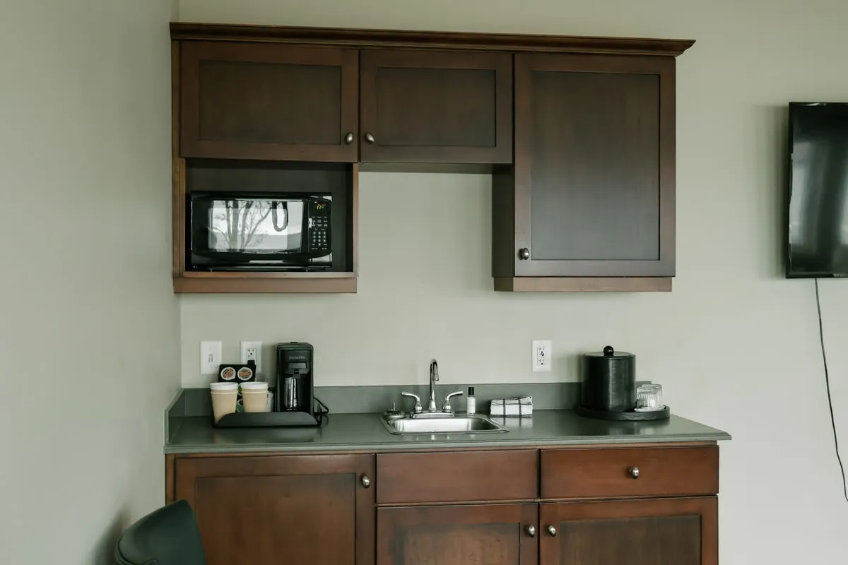 A kitchenette with dark wood cabinets, a microwave, a sink, and a coffee maker.