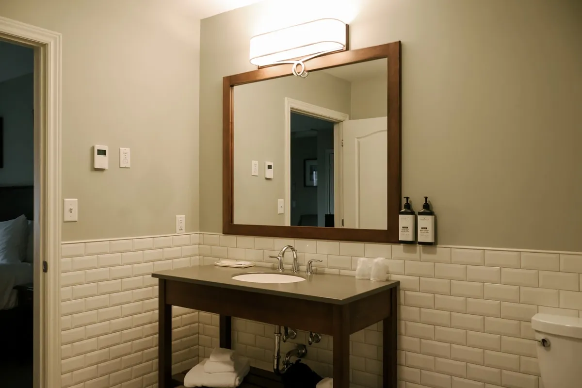 An ensuite bathroom with a wood vanity, framed mirror, and white subway tile.