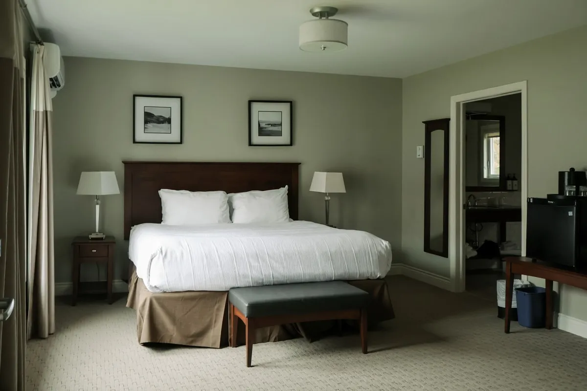 A king bedroom with bedside lamps, a bench at the foot of the bed, and an open doorway to the ensuite.