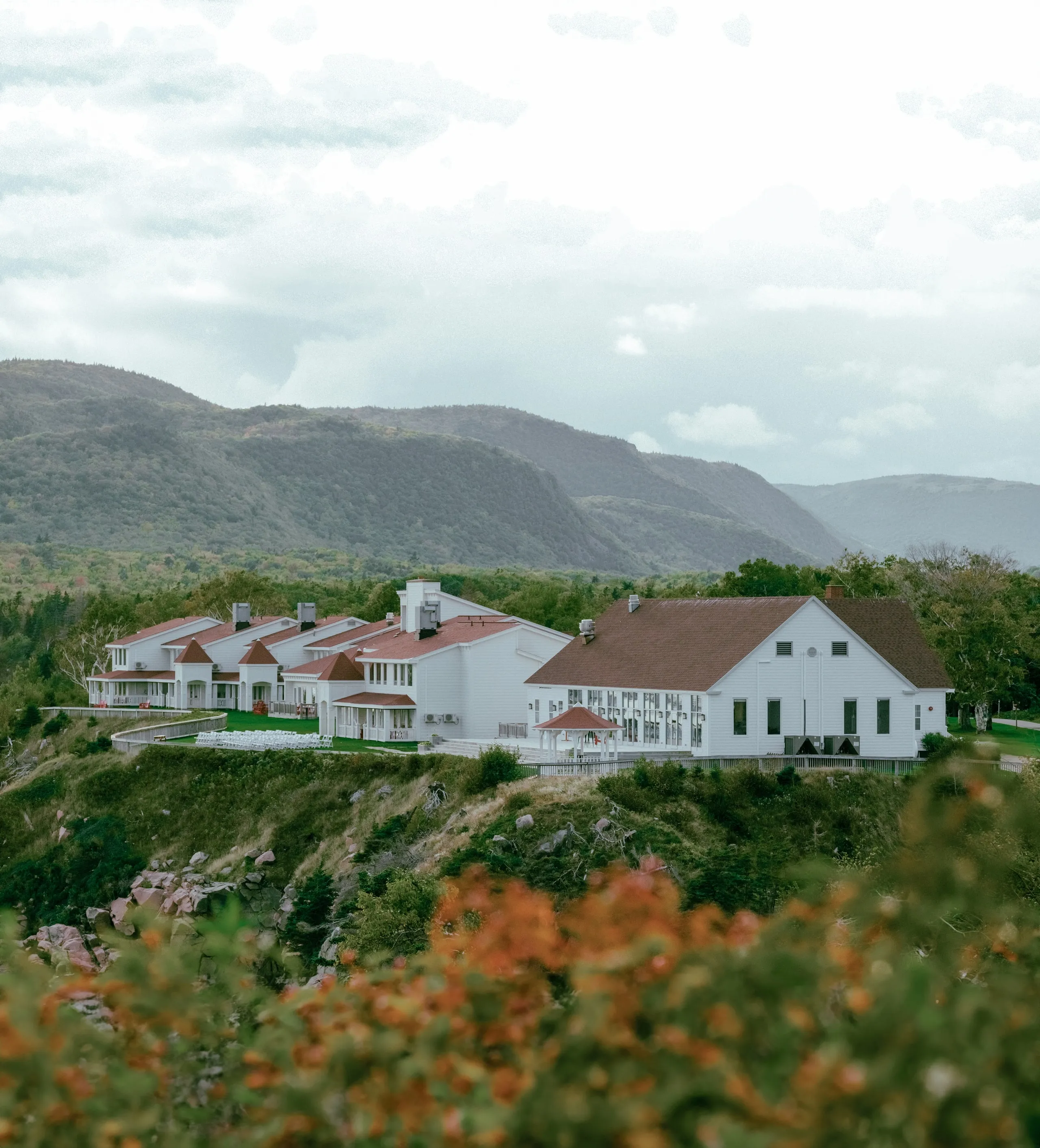 The white Keltic lodge buildings with red roofs on a grassy hillside, with forested mountains behind