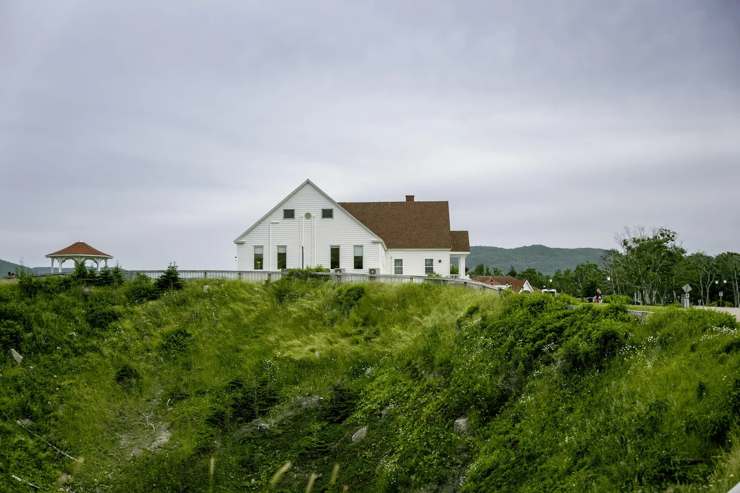 The white Keltic Lodge on a grassy bluff, with a gazebo and forested hills behind