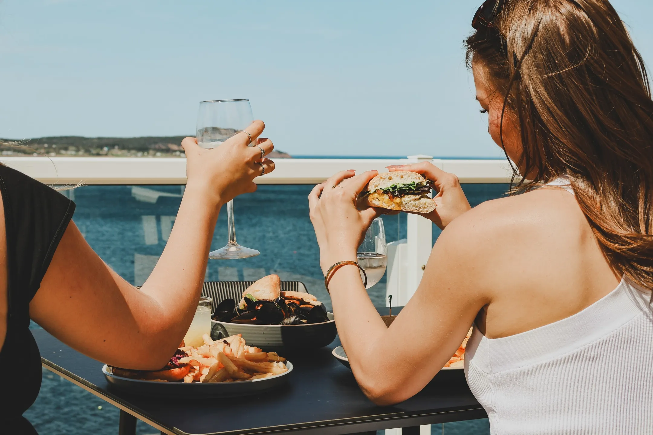 Guests dining on the oceanfront patio with a burger, fries, mussels, and wine overlooking the Atlantic.