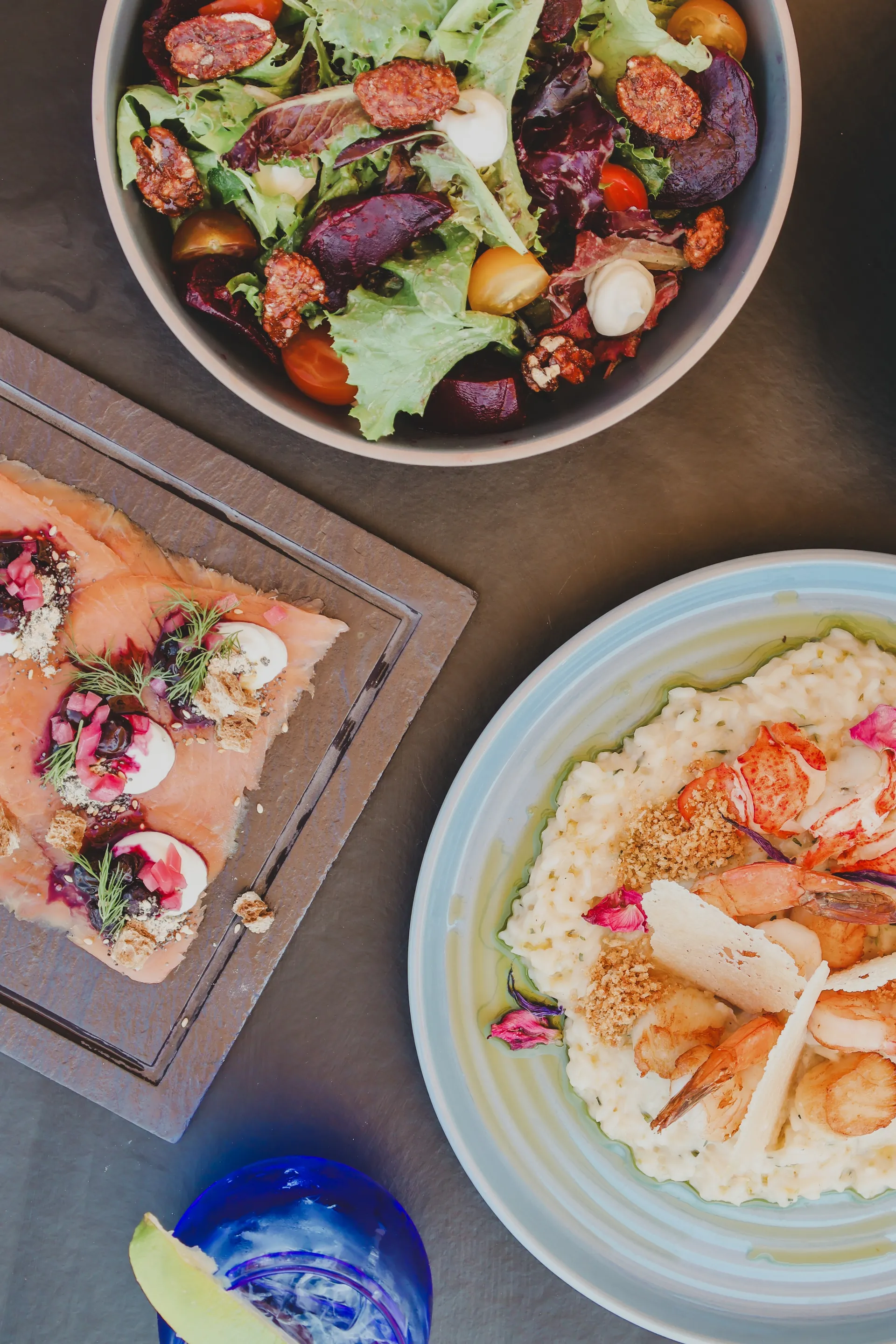 Overhead view of beet salad, smoked salmon, and lobster risotto on a dark table.