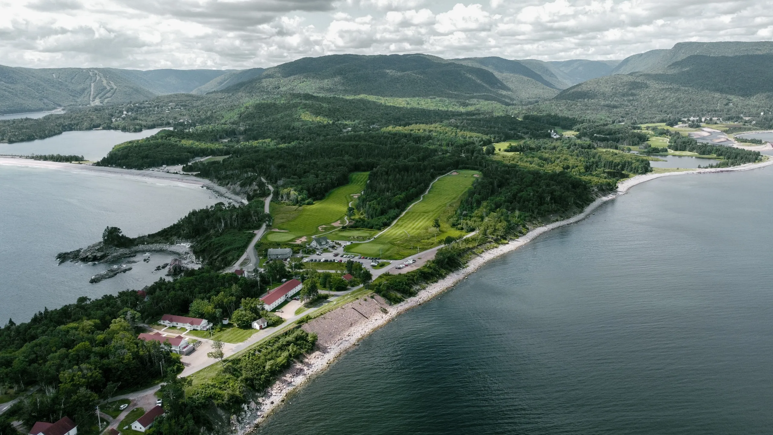 Aerial view of The Keltic Resort and Highlands Links along the Cape Breton coast with mountains beyond.