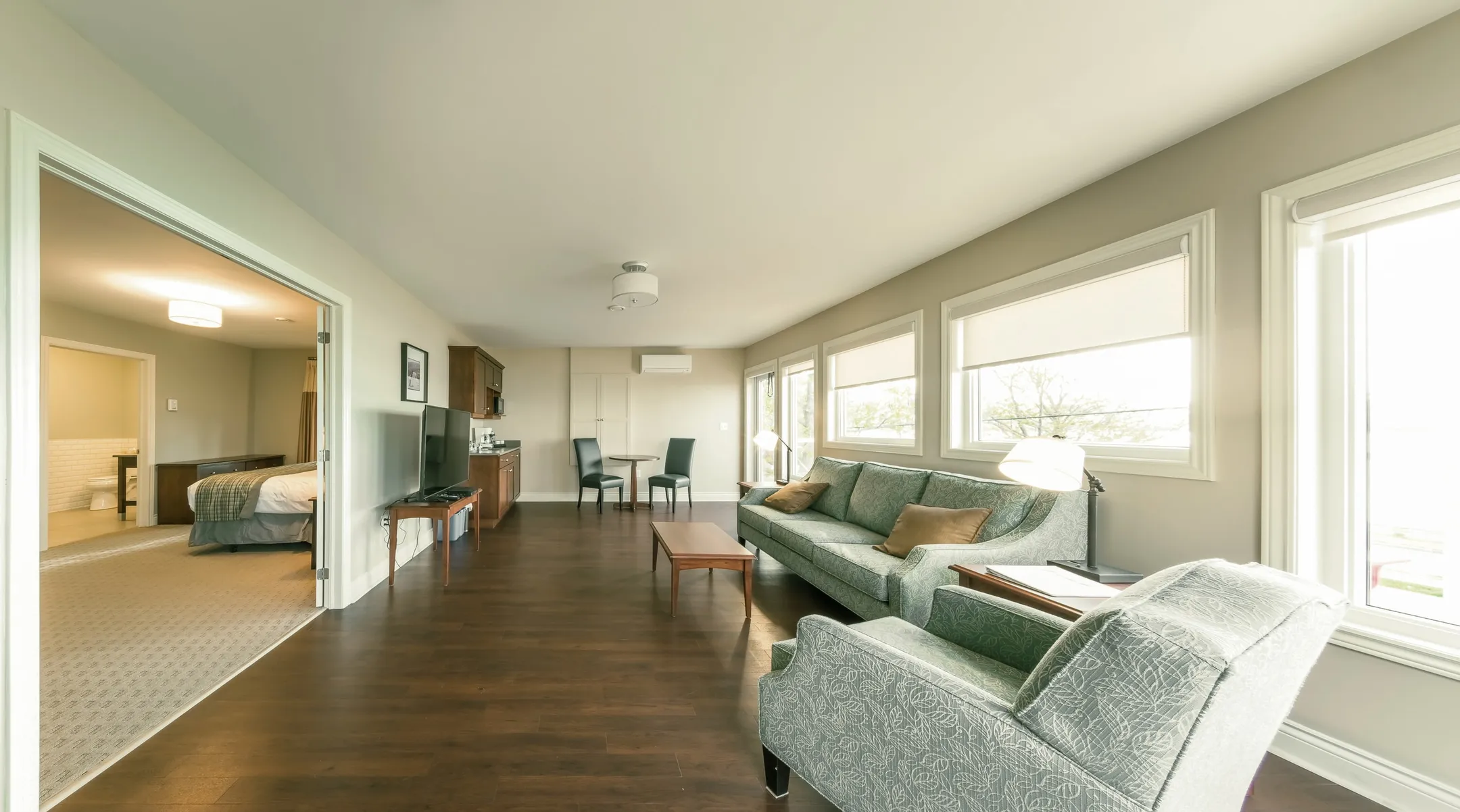 A suite living room with a sage sofa, coffee table, and windows looking onto the grounds.
