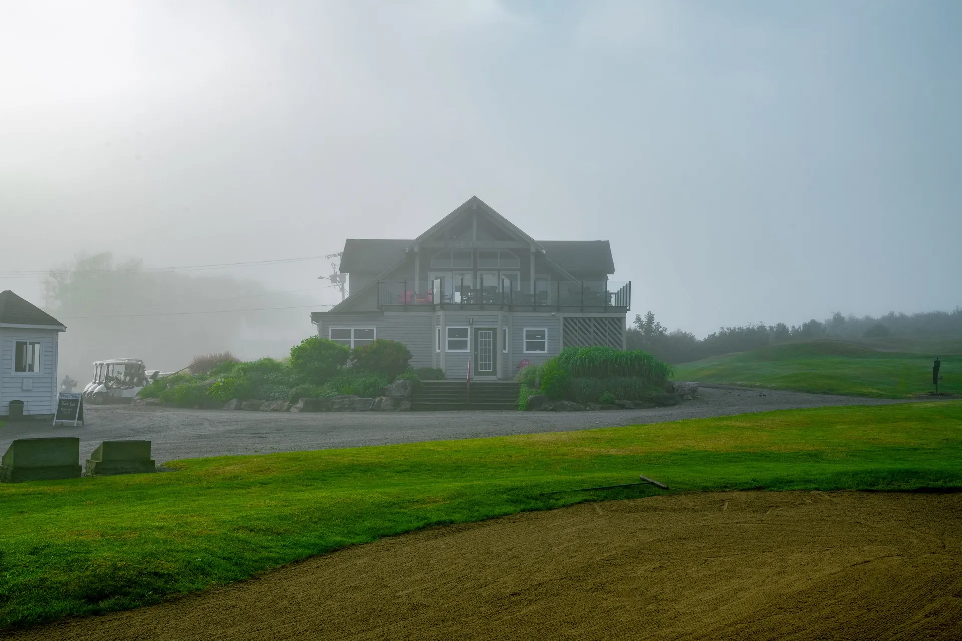 Fog-covered Highlands Links clubhouse above a green and a sand bunker.