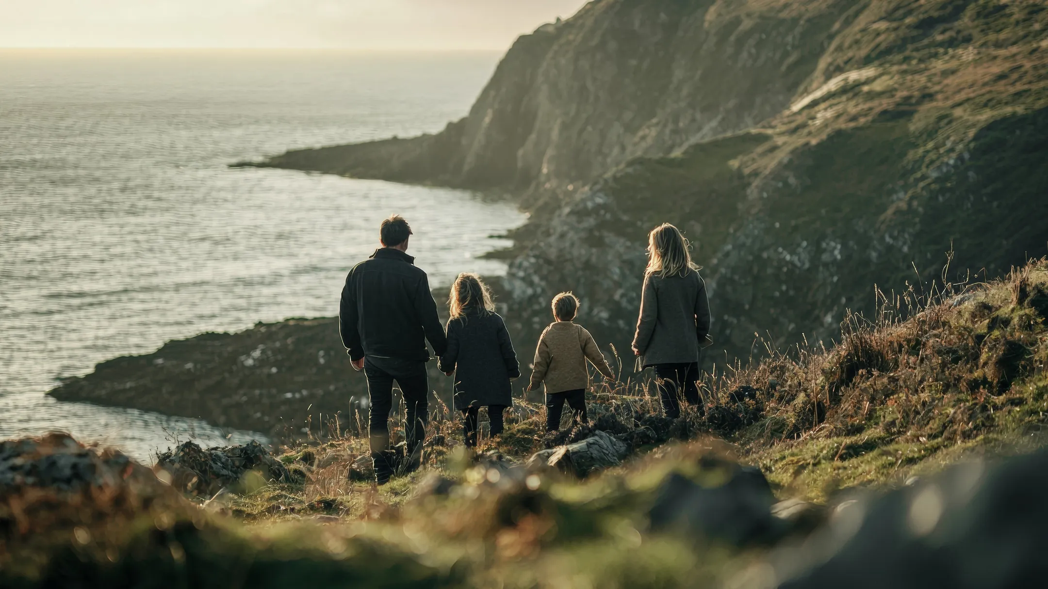 A family of four walking a grassy cliff path above the ocean