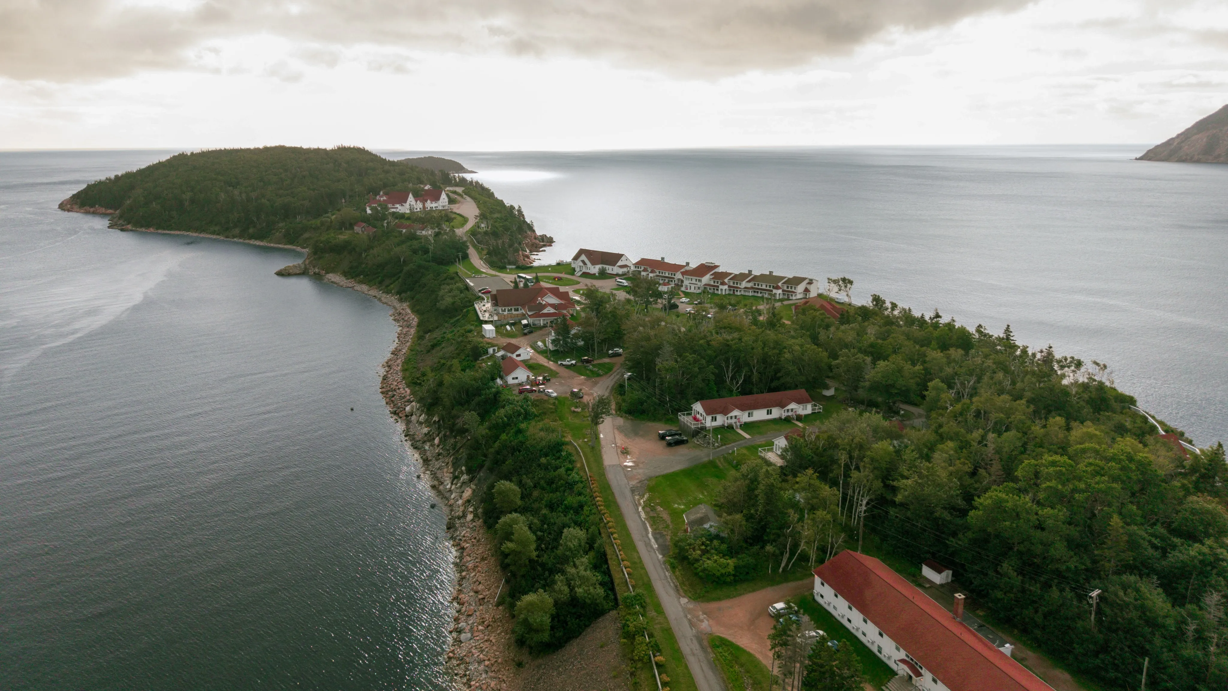 Aerial view of The Keltic Resort on the Middle Head Peninsula, red-roofed buildings along a rocky shoreline with the Atlantic beyond.