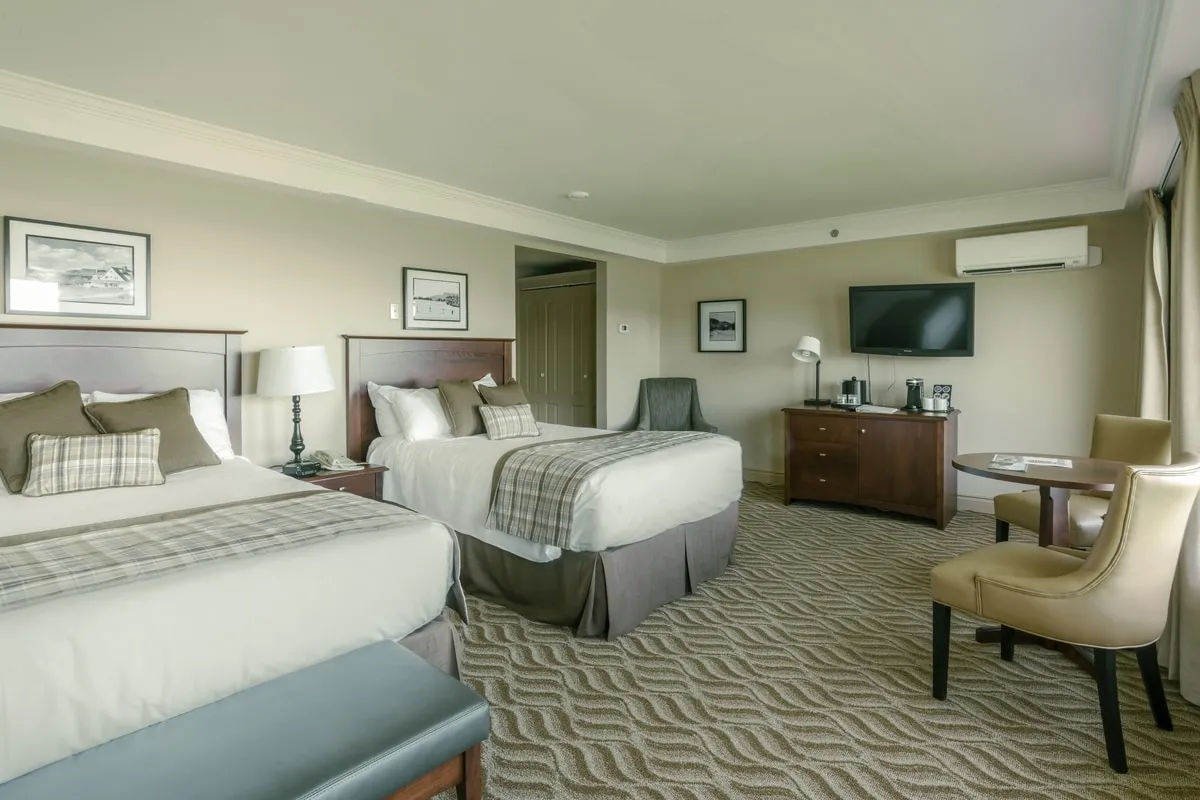 A guest room with two beds, a dresser and television, and a table with chairs beside the window.