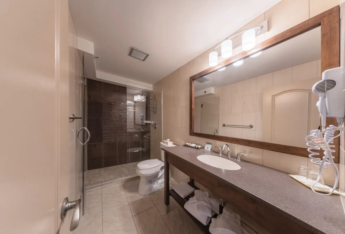 A guest bathroom with a glass shower, a wood-framed mirror, and towels under the vanity.