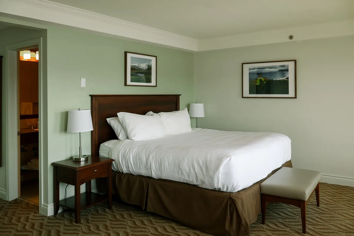 A guest room with a king bed, sage-green walls, and framed pictures above the headboard.