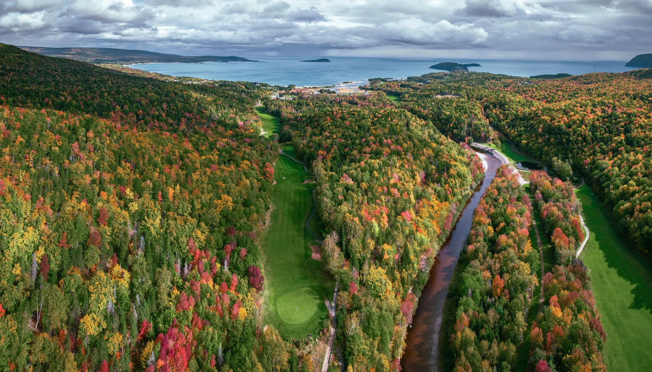 Aerial view of Highlands Links fairways winding through autumn forest toward the Atlantic.