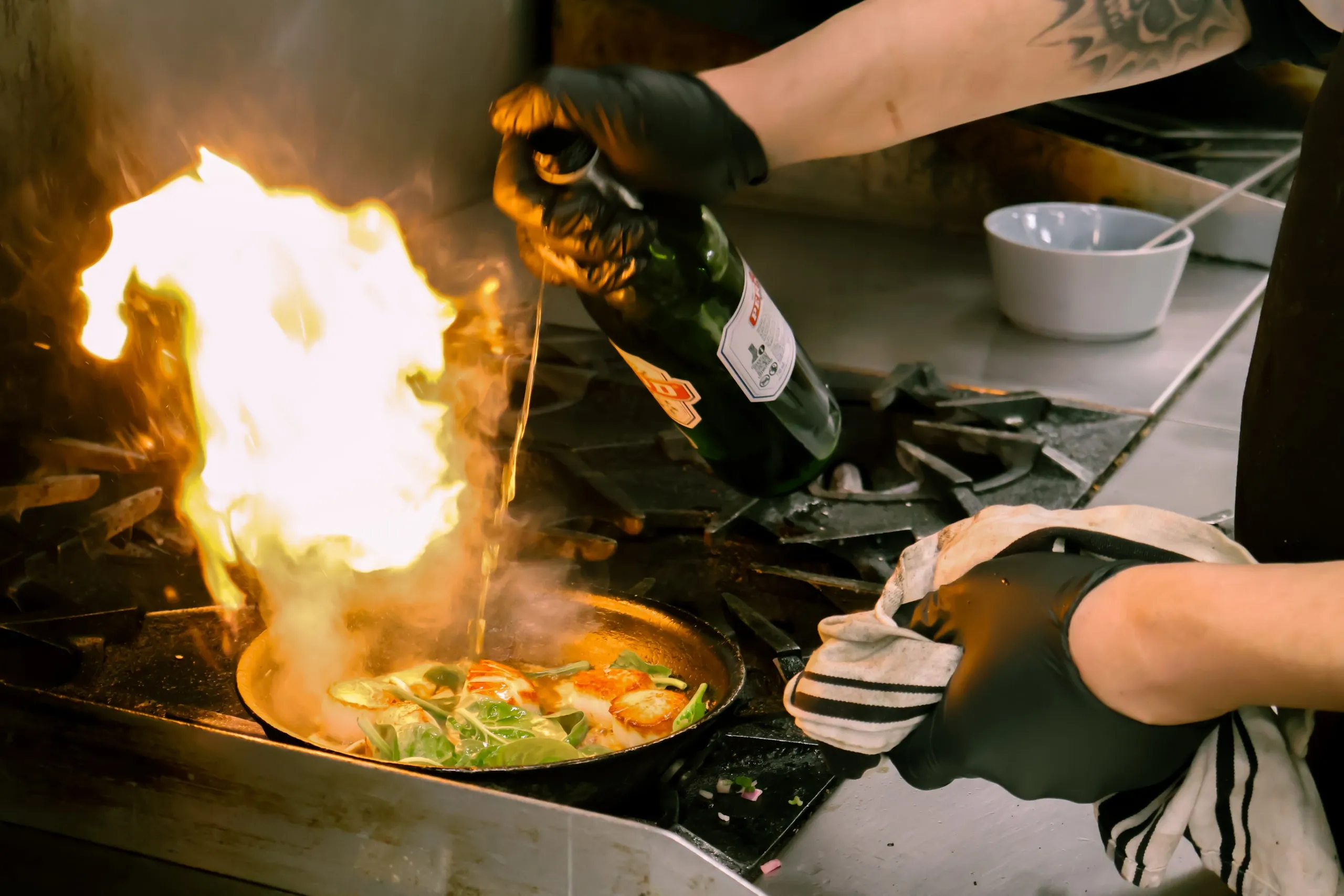 A chef flambéing scallops in a pan.