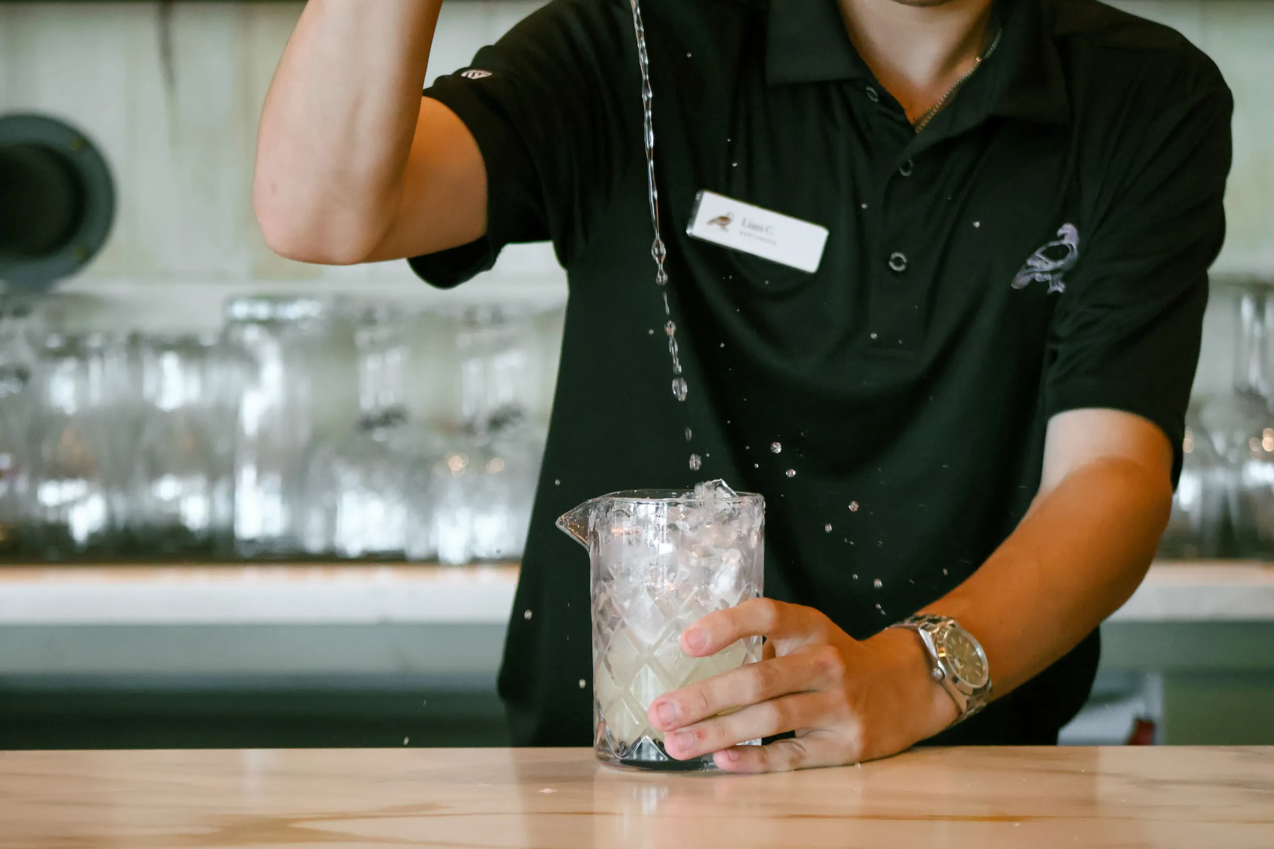 A bartender pouring a drink into a mixing glass.