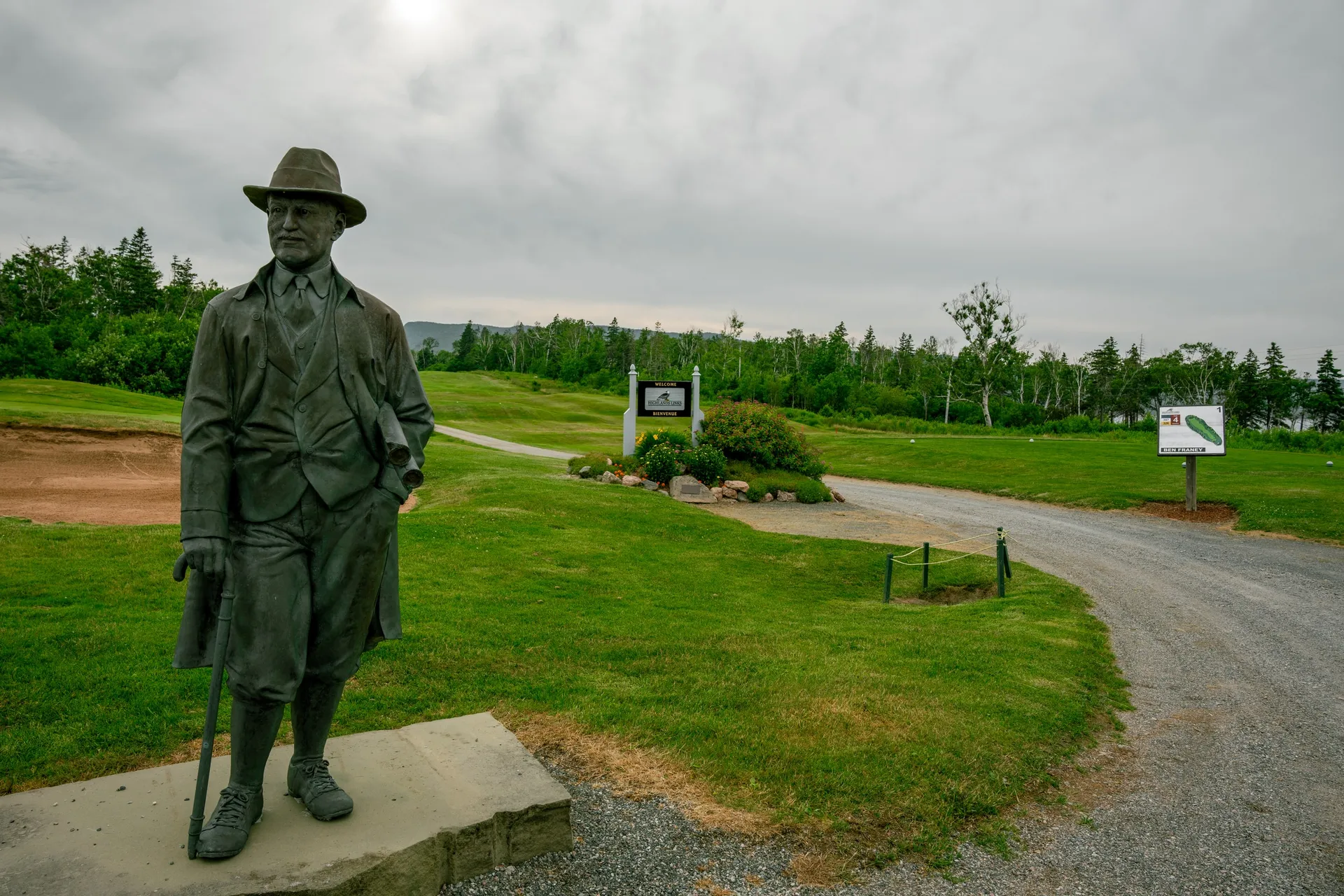 A bronze statue of Stanley Thompson overlooking the first tee at Highlands Links, with the course and Highlands beyond.