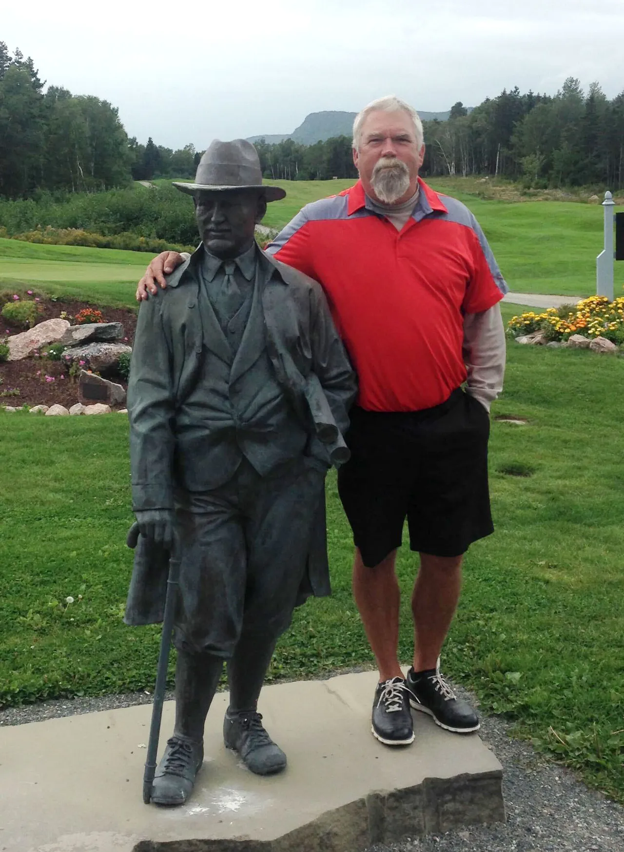Dan Lavis standing beside the Stanley Thompson statue on the golf course