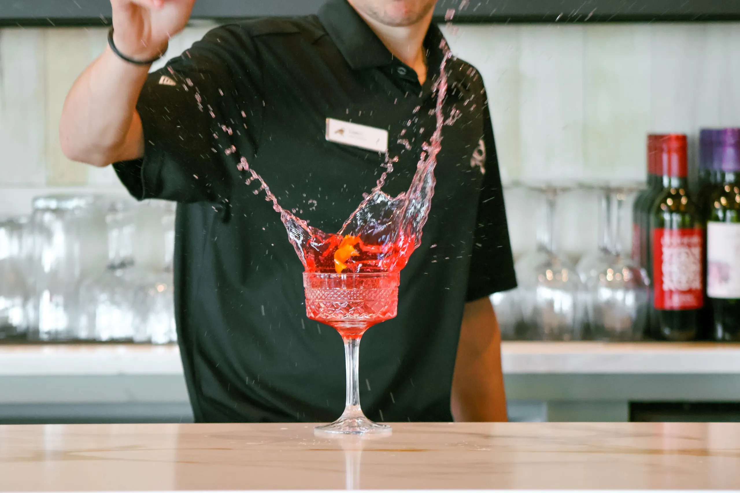 A bartender pouring a red cocktail.