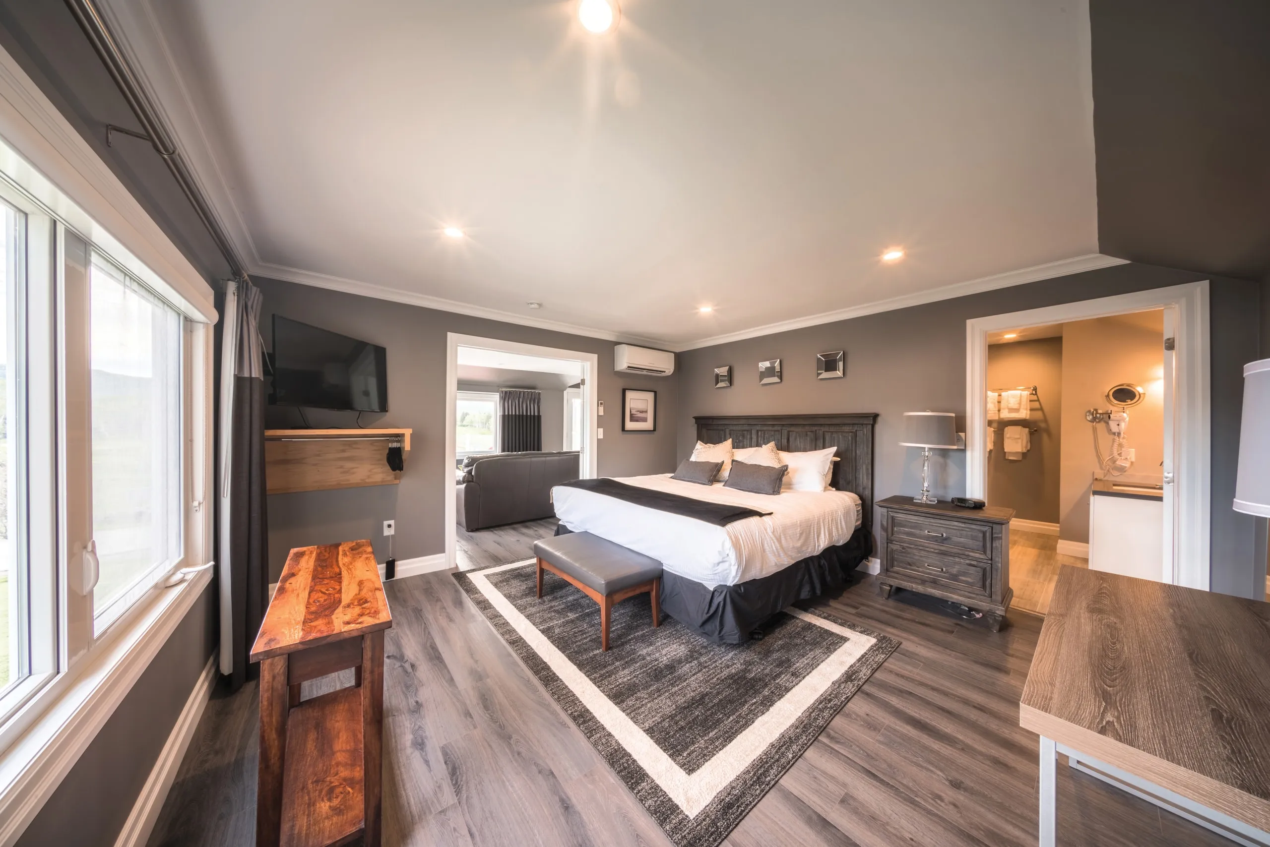 A bedroom suite with a king bed, grey walls, and doorways opening to a living area and bathroom.
