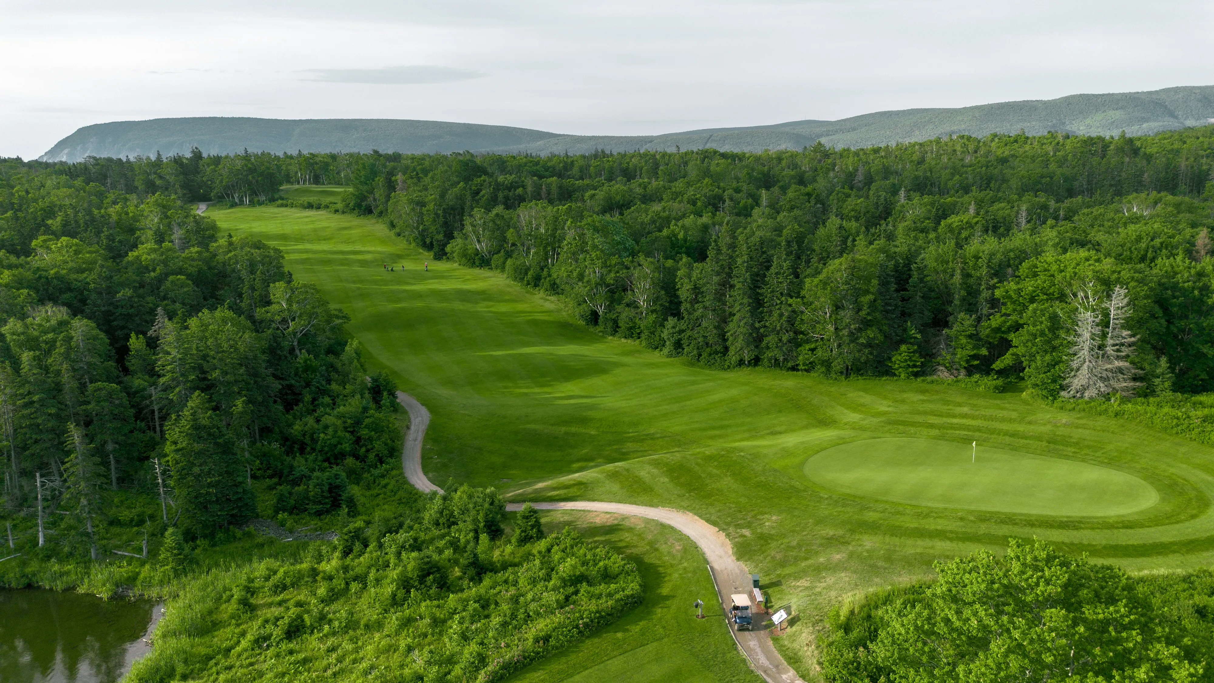 Aerial view of a Highlands Links fairway curving toward a green, with the coast beyond.