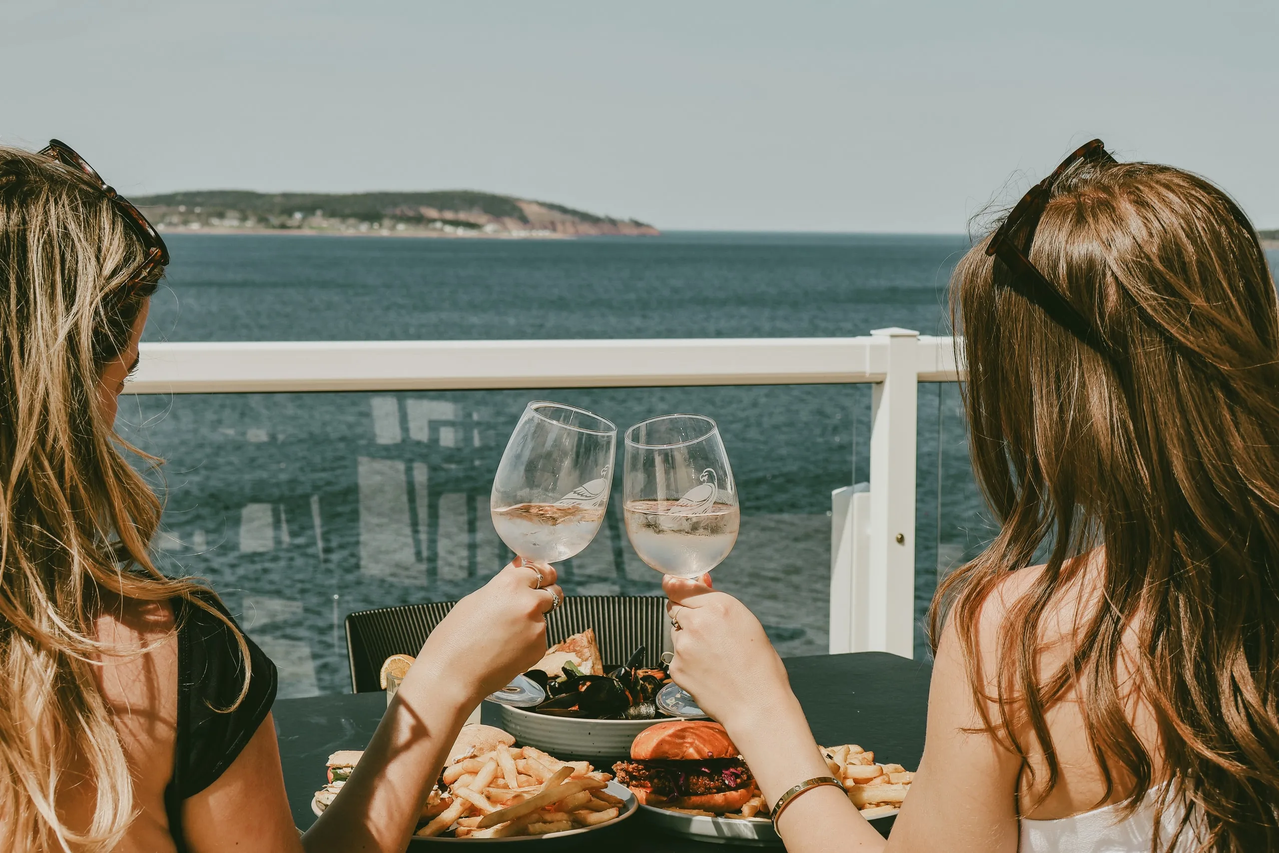 Two guests toasting with wine on the patio, looking out over the Atlantic.