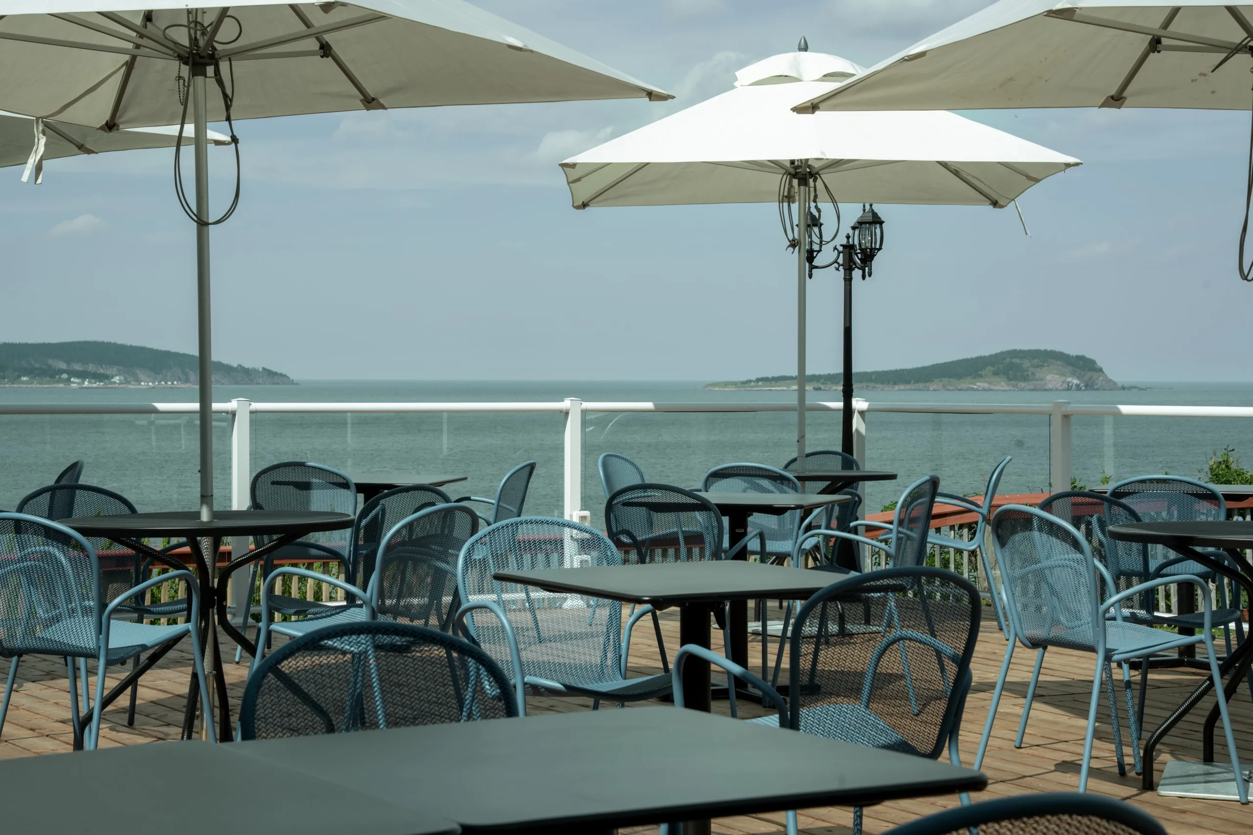 Blue patio chairs and white umbrellas on the deck above the water.
