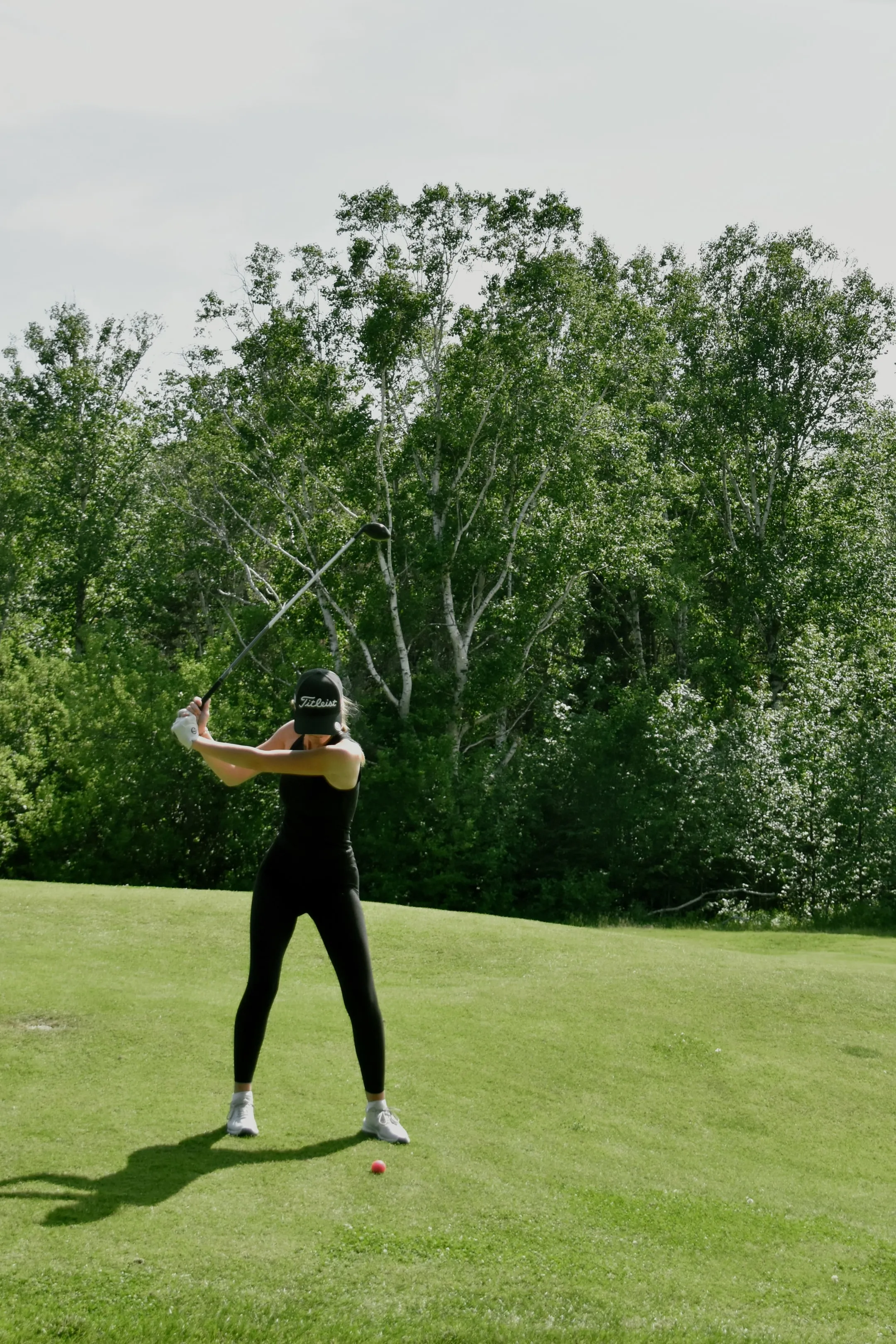 A golfer in black mid-swing on a green fairway, with a pink ball on the grass.