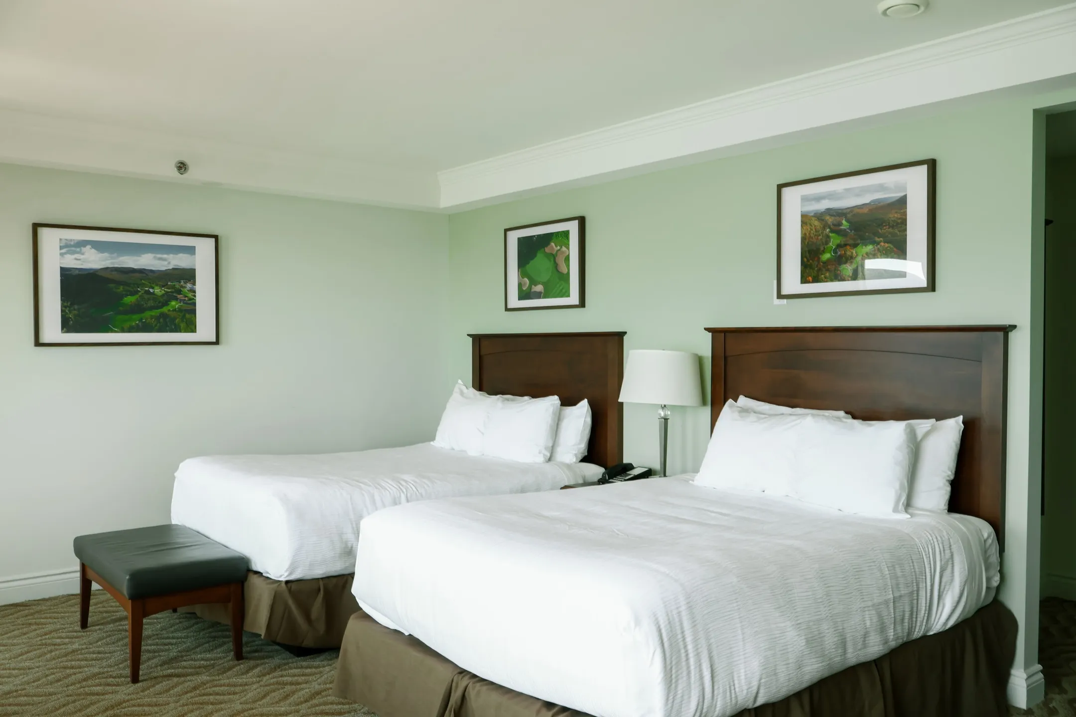 A guest room with two beds, sage-green walls, and framed landscape photographs.