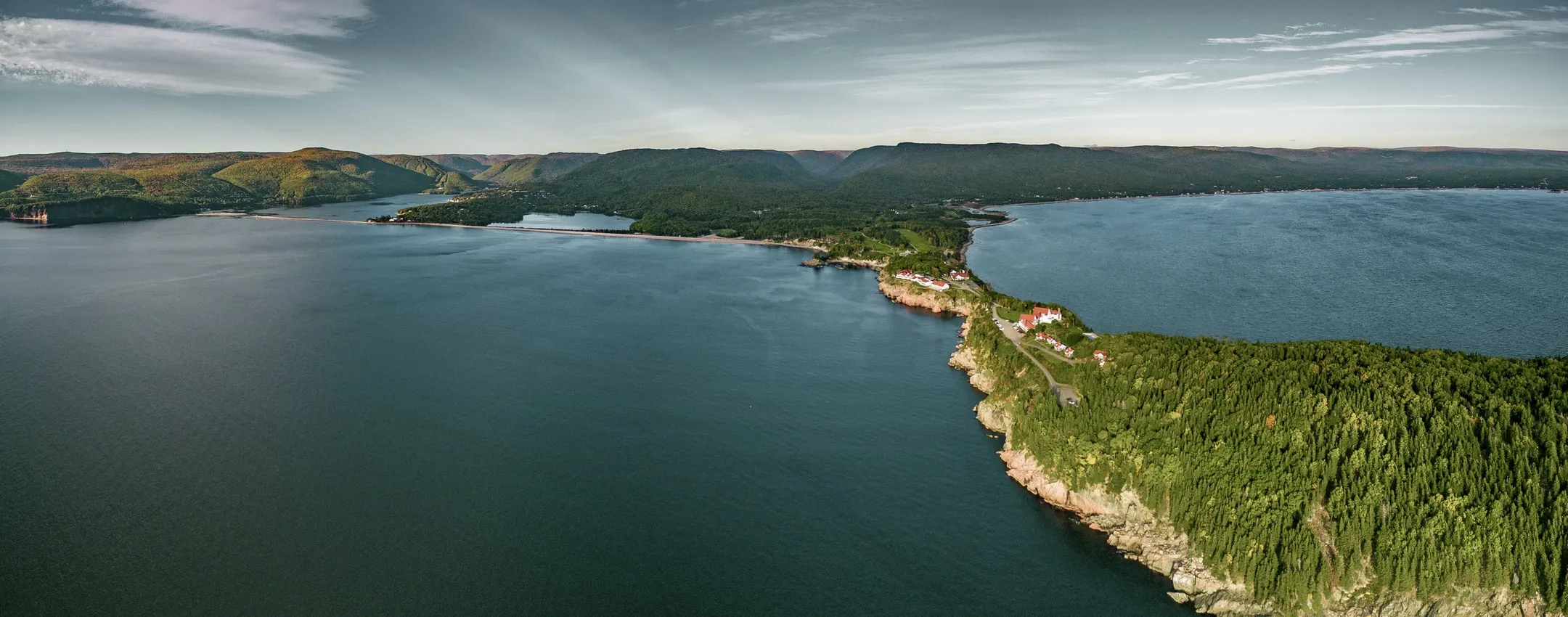 An aerial view of the forested coastline, a sandy beach, and mountains across the water.