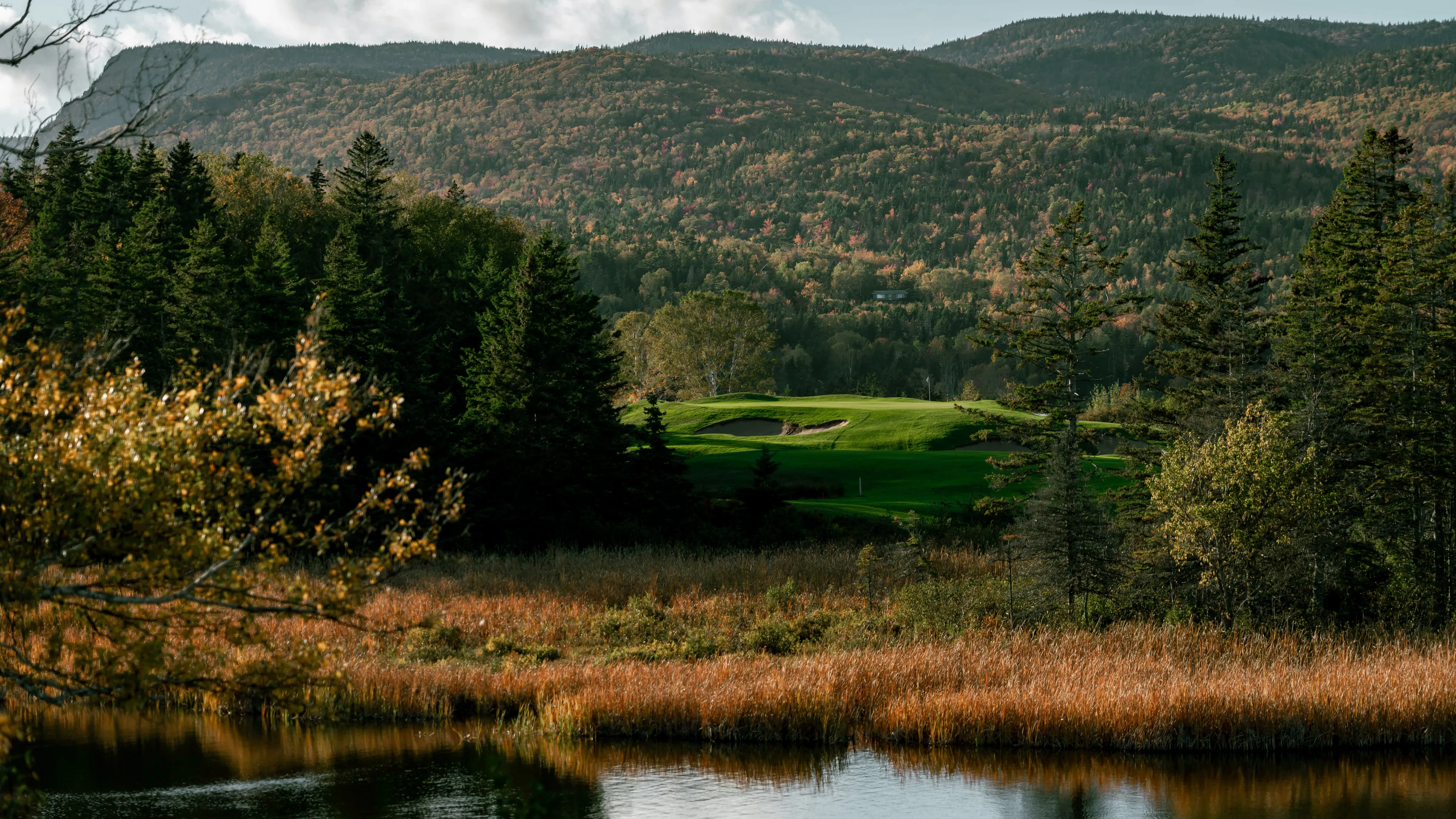 A Highlands Links green beside still water, with autumn colour on the mountains.