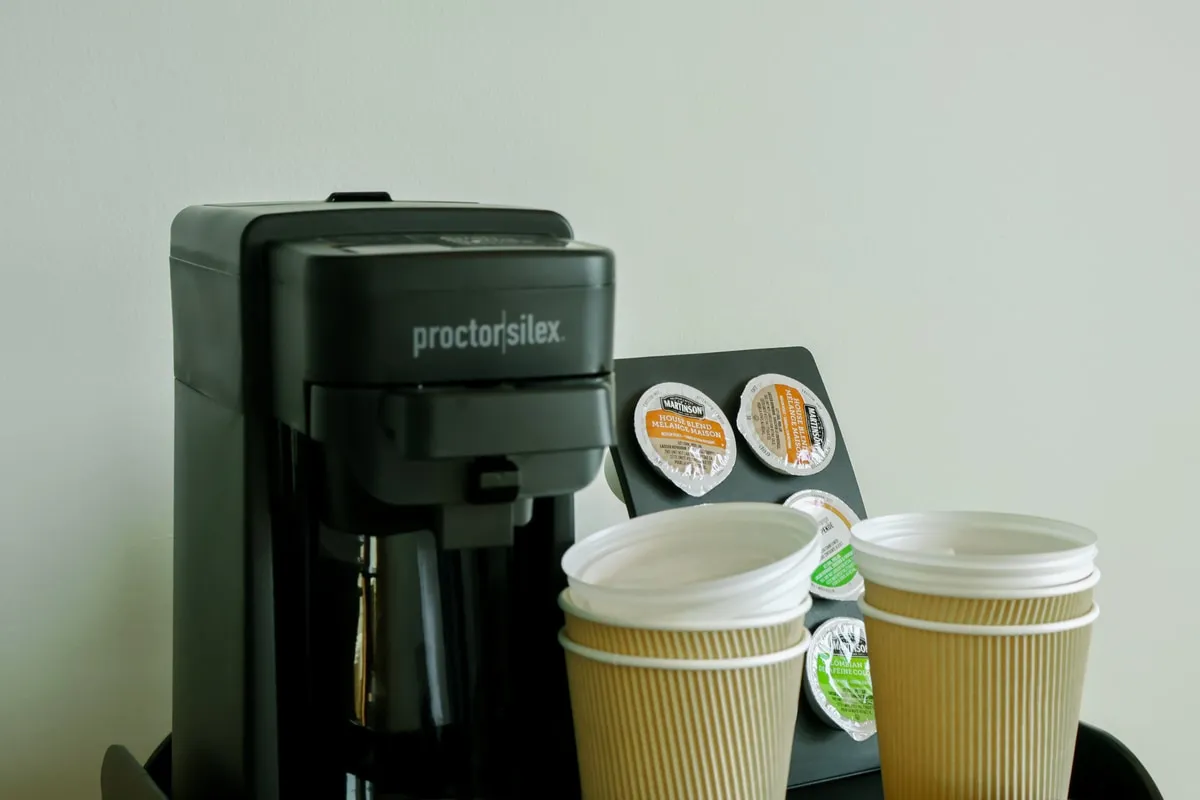 A coffee maker with stacked paper cups and a rack of single-serve coffee pods.