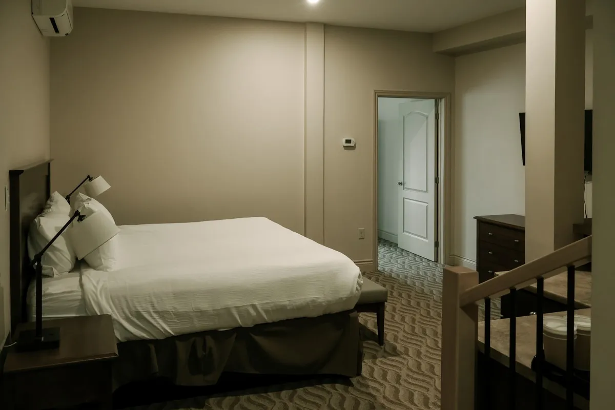 A studio suite bedroom with a king bed, an open white door, and a stair rail in the foreground.