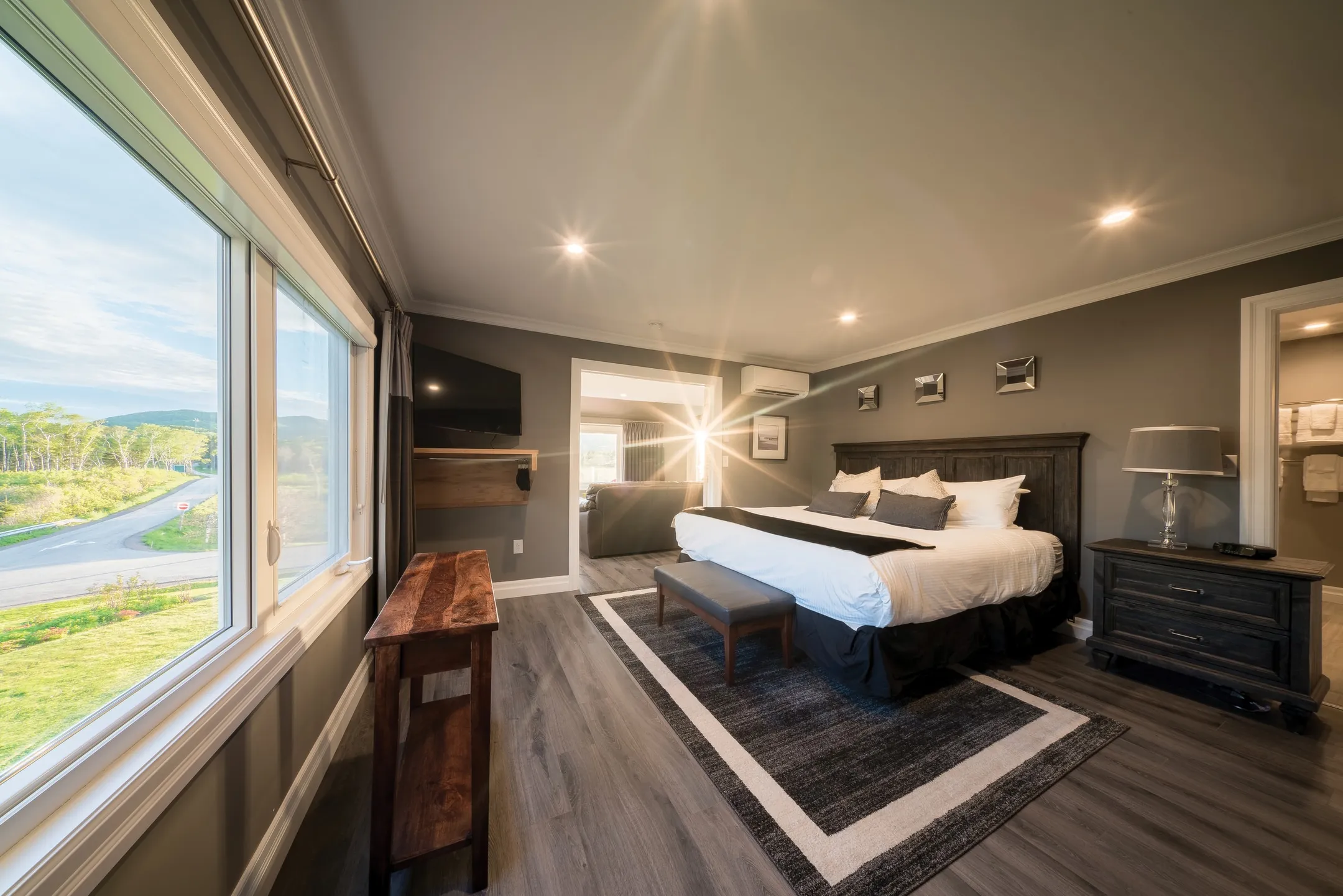 A one-bedroom suite with a dark wood bed, a bench at the foot, and windows looking onto the grounds.