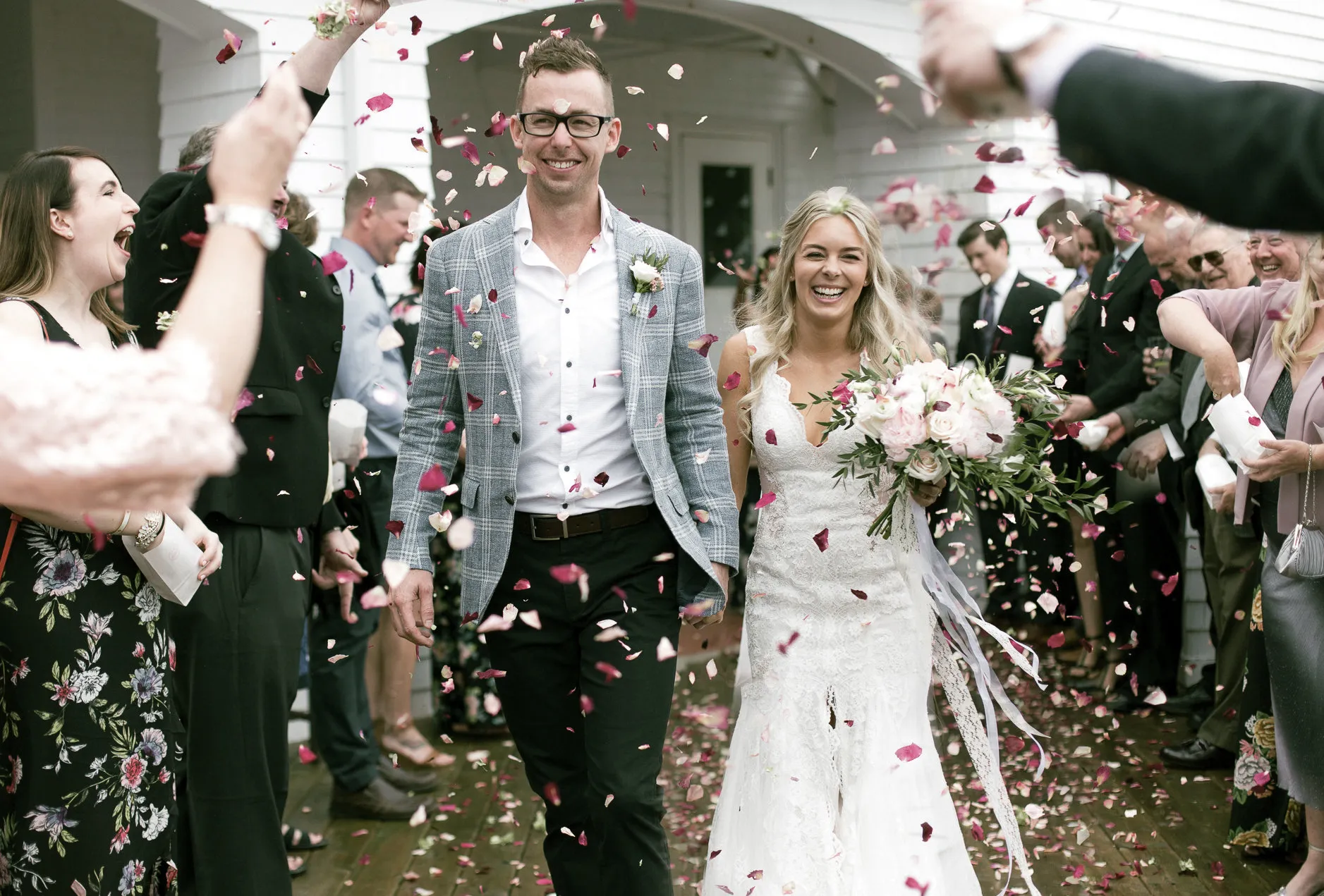 A bride and groom walk through falling confetti with their wedding guests.